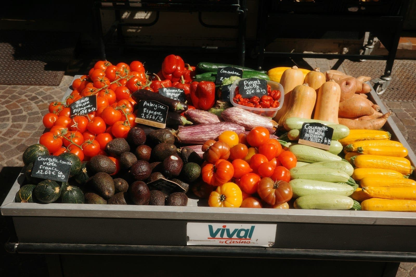Свежие продукты, включая помидоры, кабачки и перцы, разложенные на прилавке продавца на уличном рынке под солнечным светом.