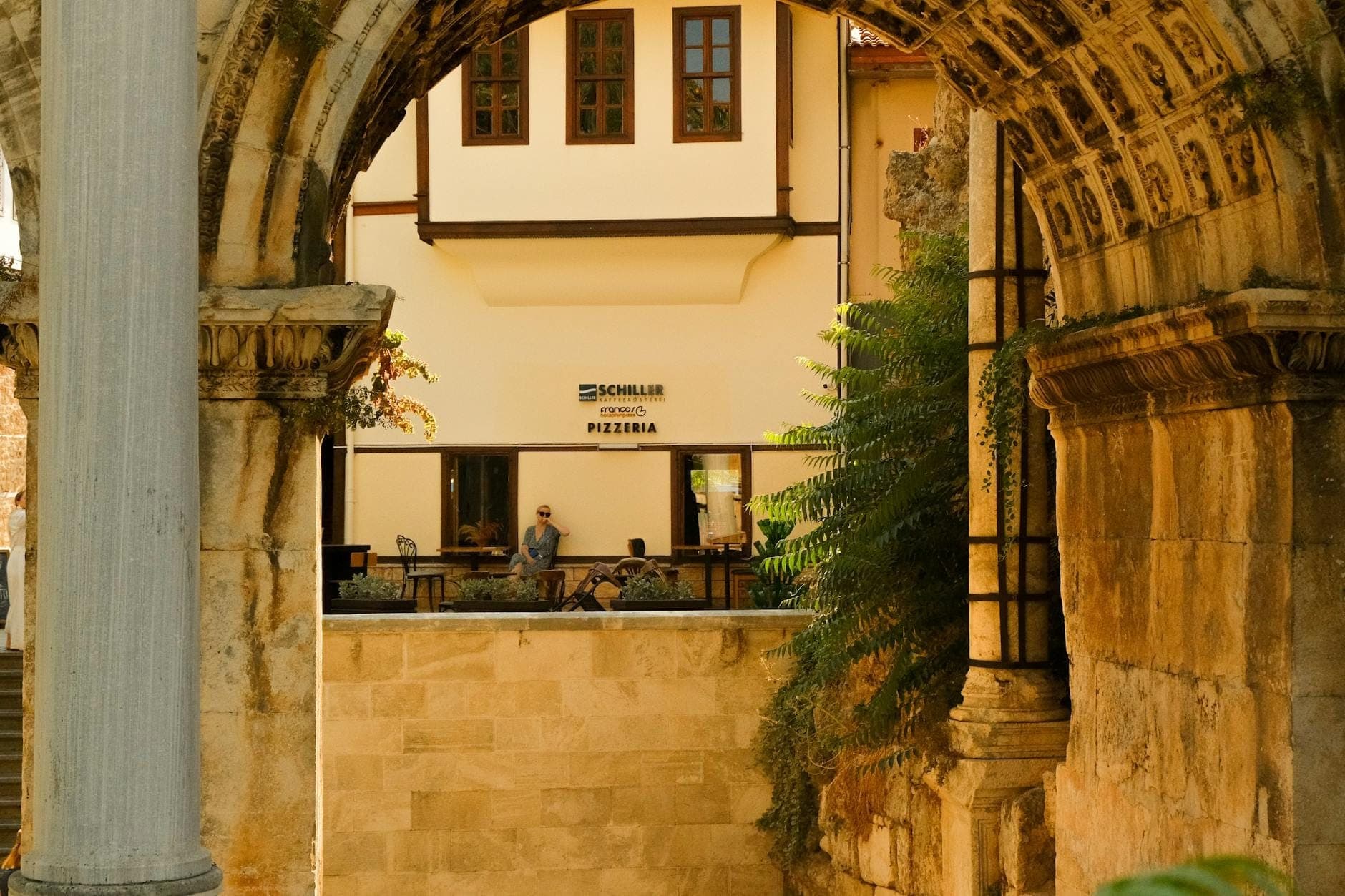 Blick durch die Steinbögen des Hadrianstor auf ein osmanisches Haus in Antalyas Altstadtviertel Kaleiçi an einem sonnigen Tag.
