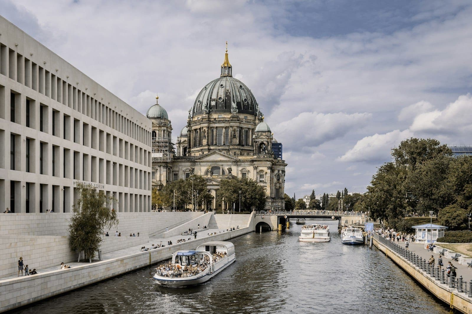 Vista del Duomo di Berlino sull'Isola dei Musei con barche sul fiume Spree e edifici moderni a sinistra.