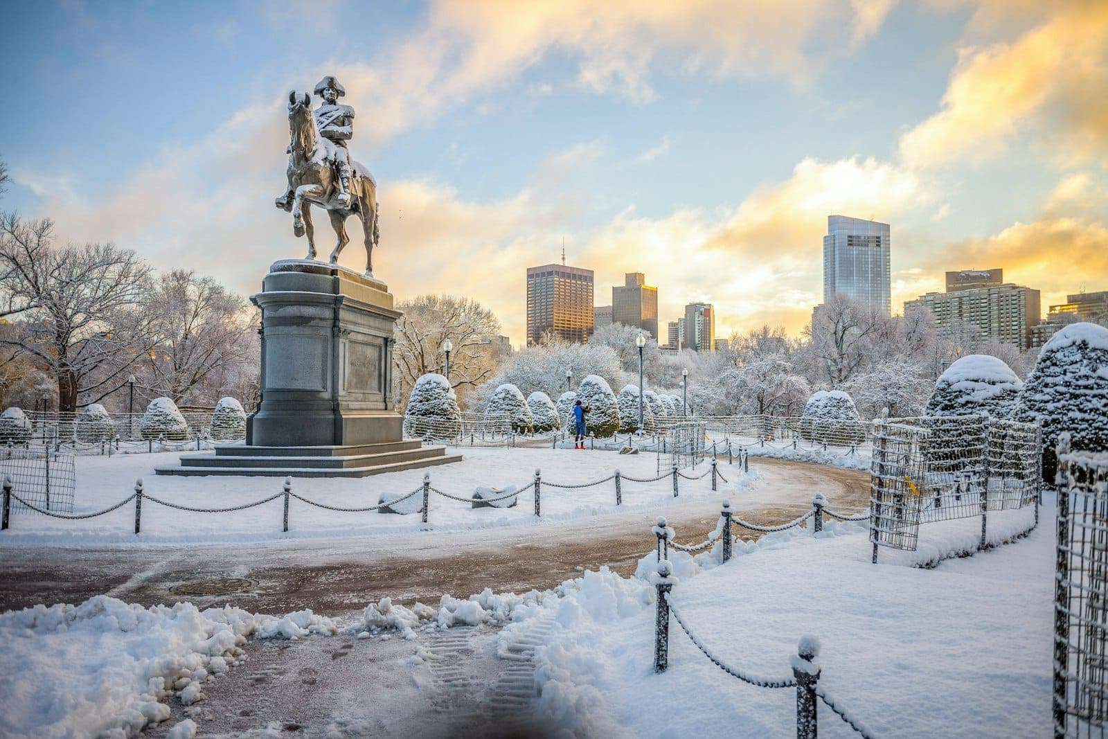 Boston Public Garden enneigé avec la statue équestre de George Washington, la skyline de la ville et un ciel d'hiver au coucher du soleil.