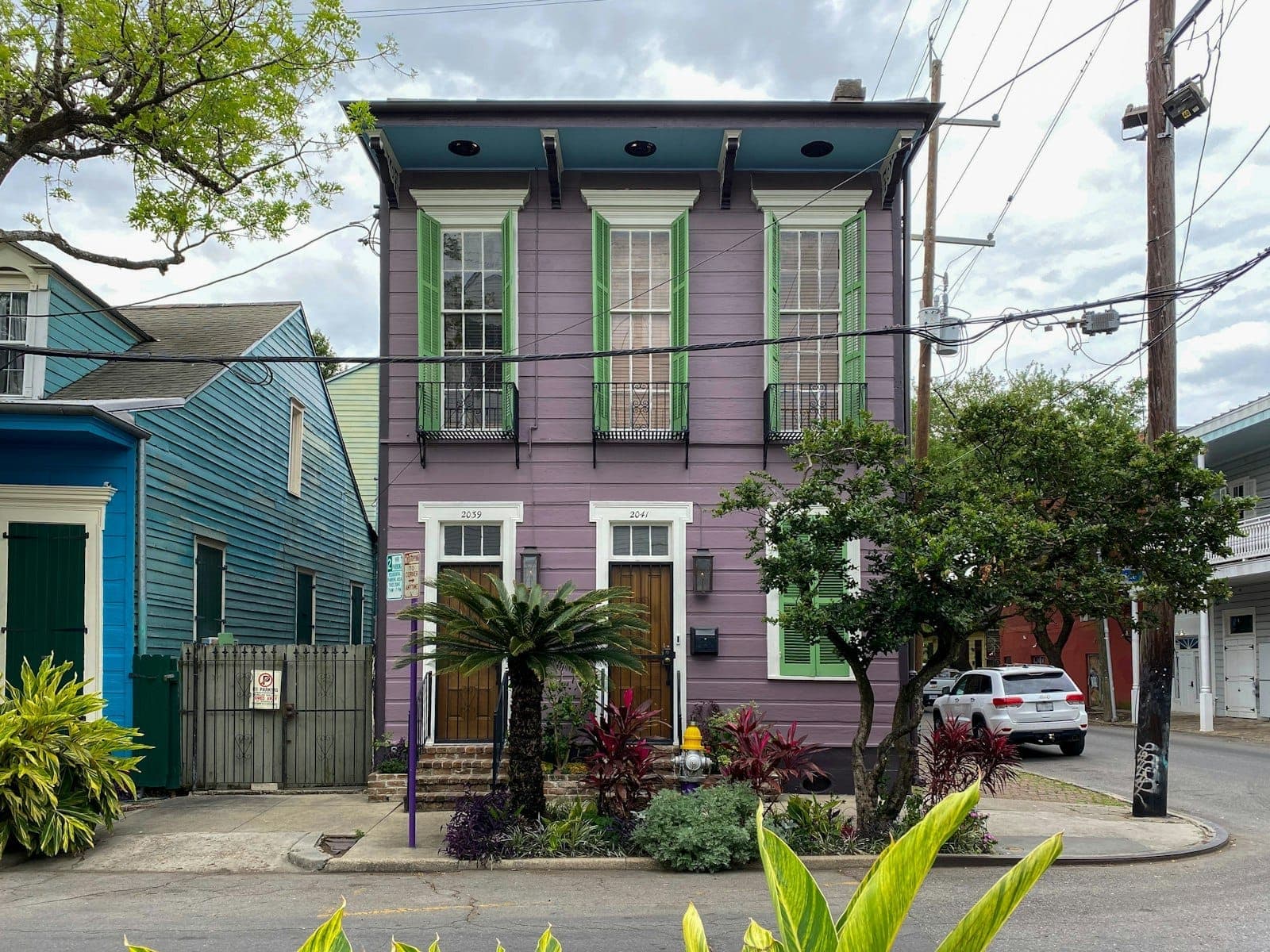 Ein klassisches Haus im Garden District von New Orleans, lila gestrichen mit grünen Zierleisten, üppigem Vorgarten und hohen Fenstern an einer baumgesäumten Straße.