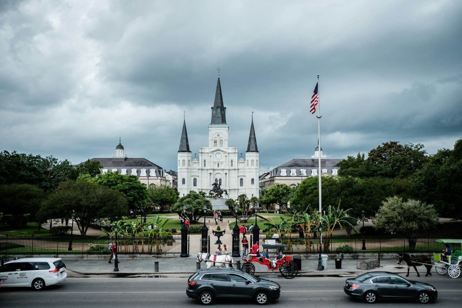 Weitwinkelansicht des Jackson Square und der St. Louis Cathedral mit den markanten Türmen und dem Reiterstandbild, Autos und einer Pferdekutsche im Vordergrund.