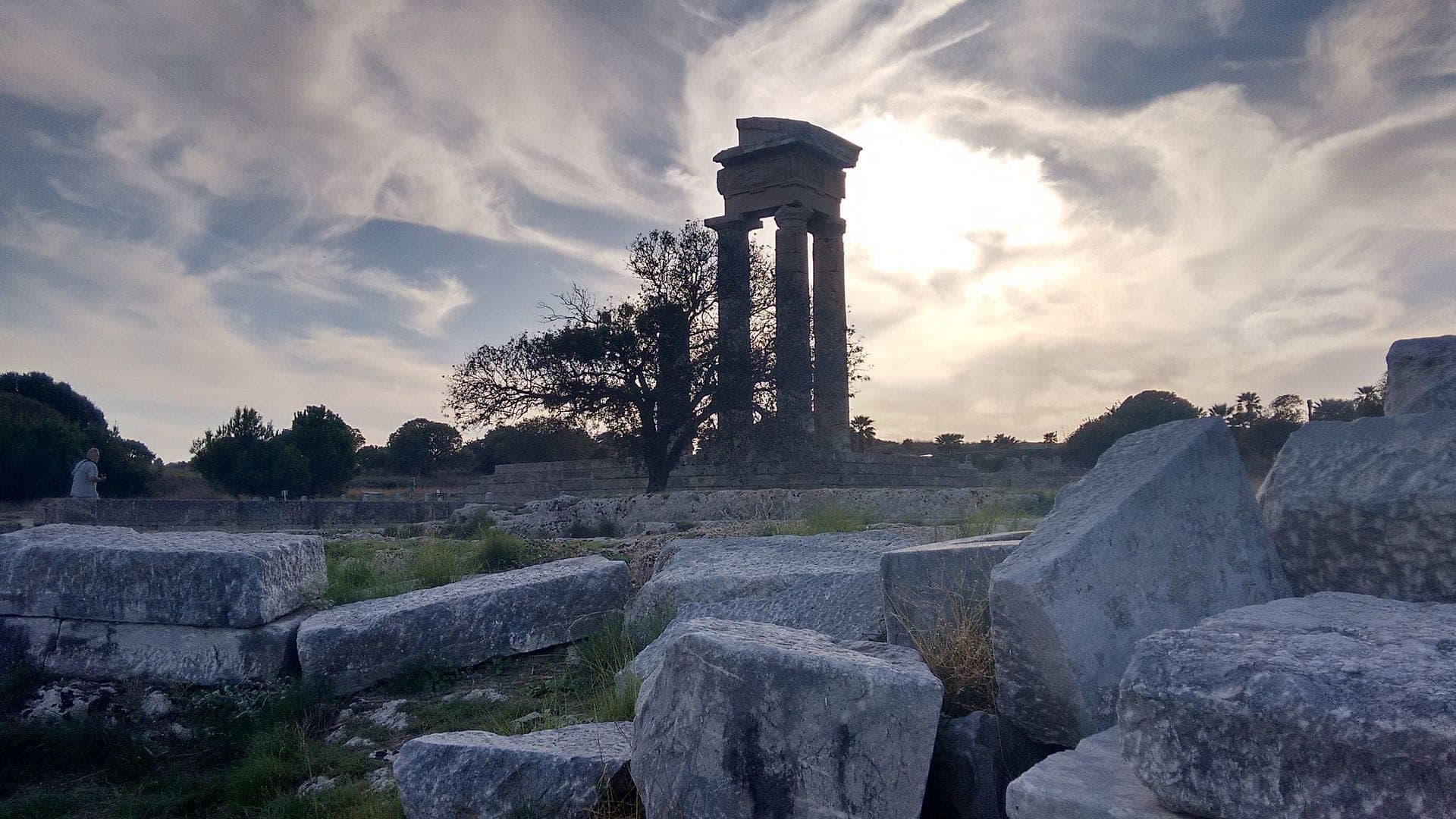 Ruines du Temple d'Apollon à l'Acropole de Rhodes, avec de grands blocs de pierre, des arbres et des nuages spectaculaires dans la lumière de fin d'après-midi.