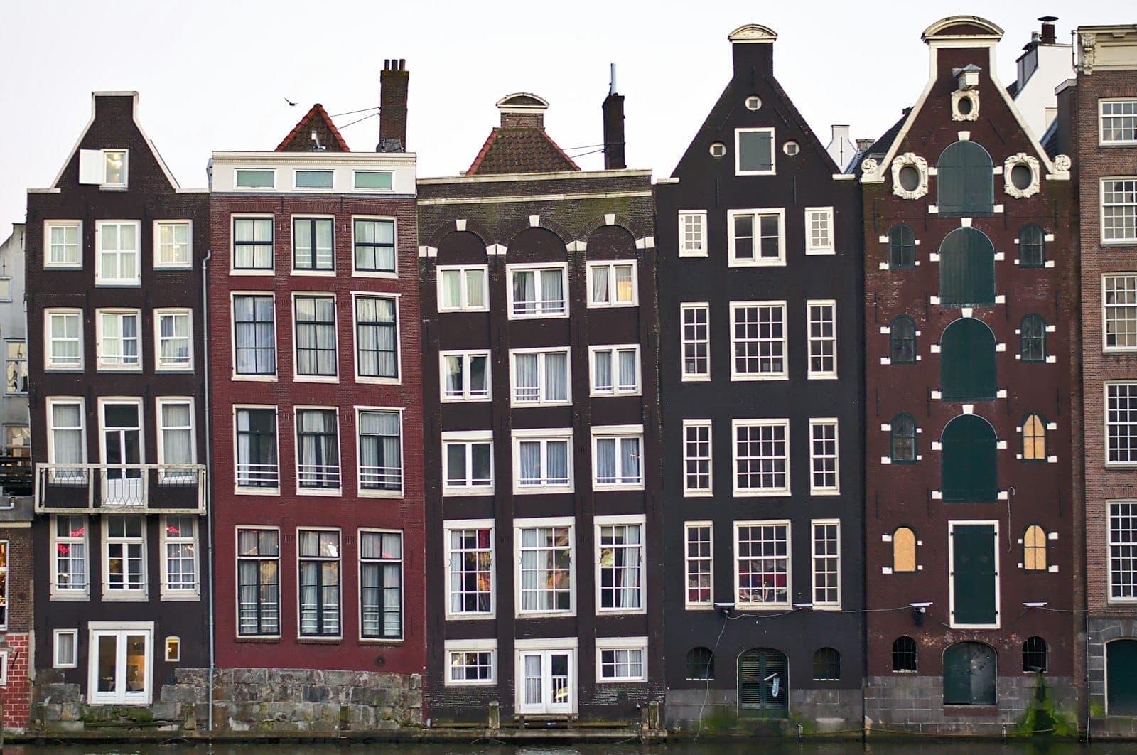 Nahaufnahme der Amsterdamer Grachtenhäuser mit schmalen, hohen Fassaden und verschiedenen Giebeln, die sich im Wasser spiegeln.