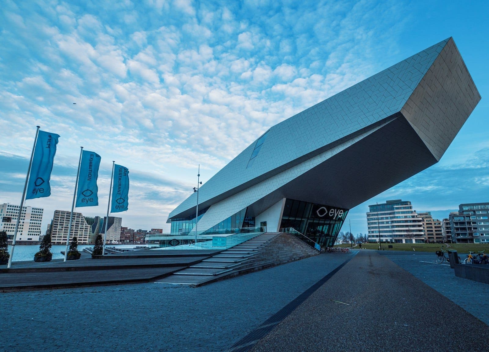 Beeindruckende moderne Architektur des Eye Filmmuseums am Amsterdamer IJ-Ufer, mit seiner kantigen weißen Fassade und den umliegenden zeitgenössischen Gebäuden unter blauem Himmel.