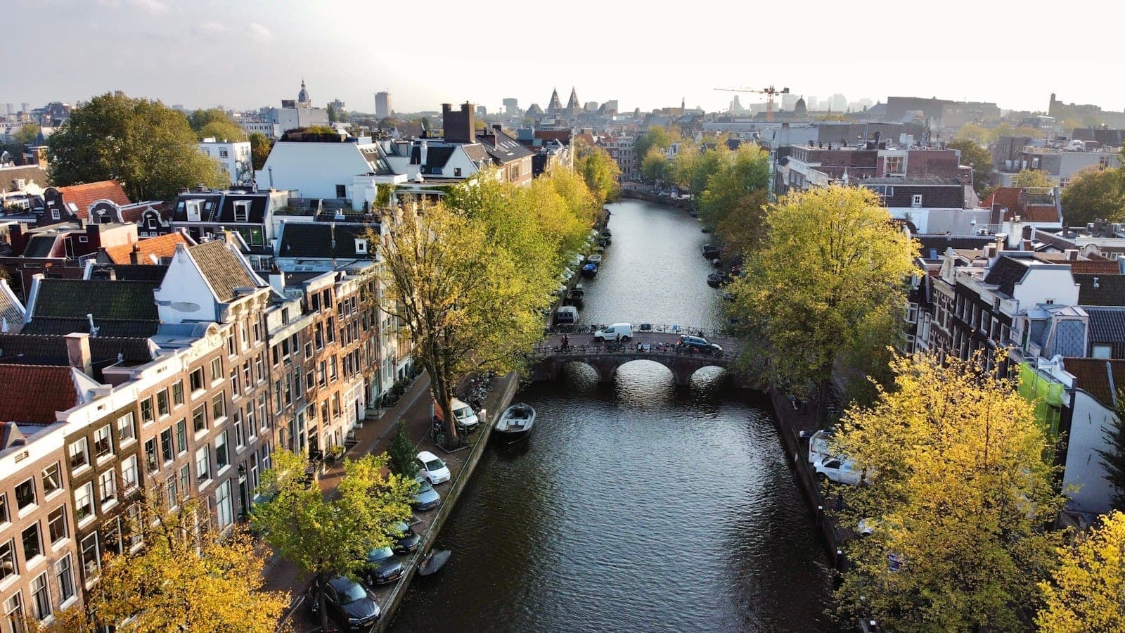 Luftaufnahme des Canal Ring von Amsterdam mit historischen Gebäuden und Brücken entlang des geschwungenen Wasserwegs, die das ikonische Stadtbild zeigt.