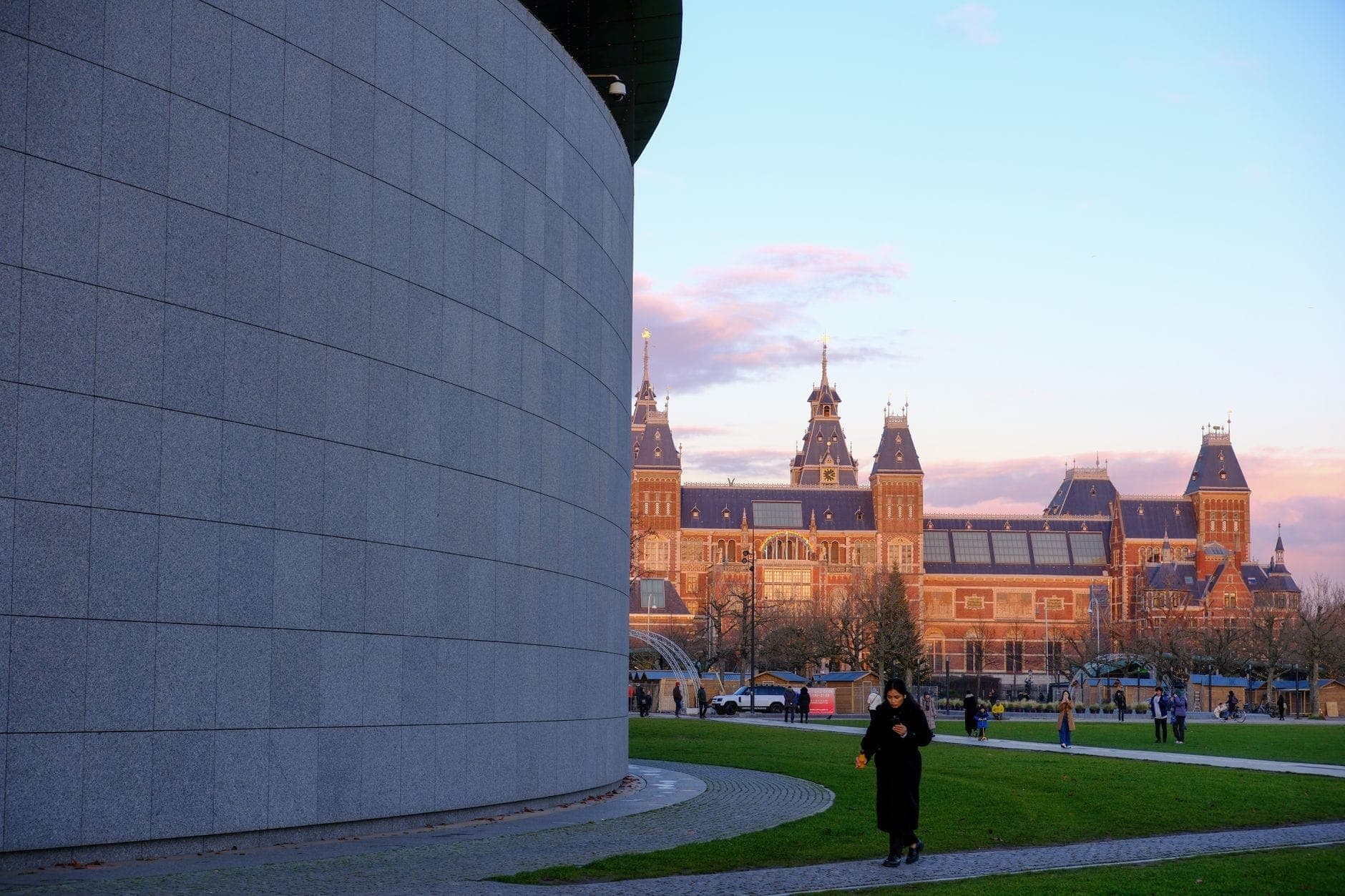 Blick über den Museumplein mit der geschwungenen Wand des Van Gogh Museums im Vordergrund und dem Rijksmuseum im Hintergrund an einem klaren Tag.