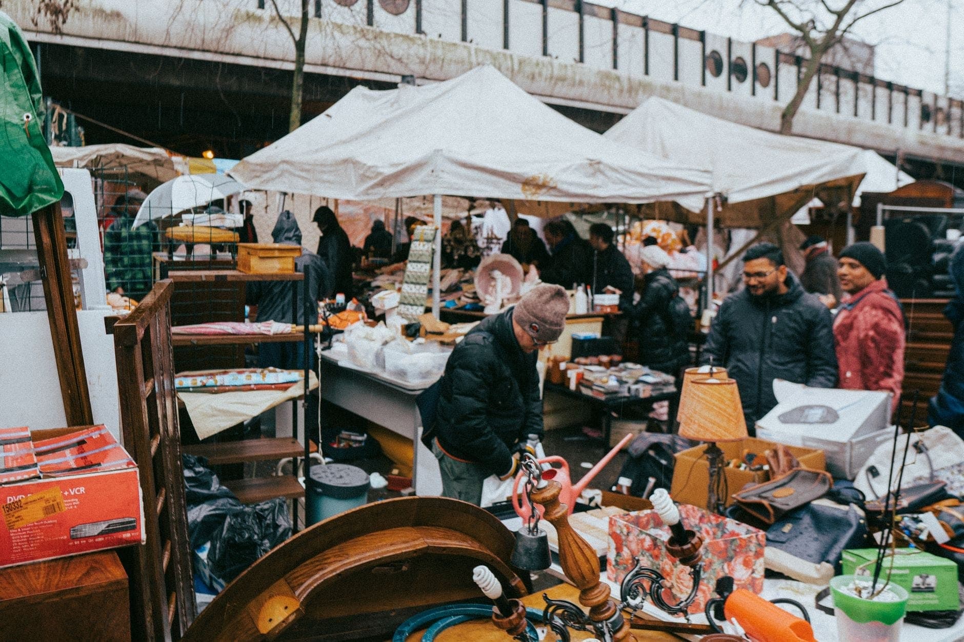 Belebter Flohmarkt im Freien in Amsterdam, mit Käufern, die unter weißen Zelten Secondhand-Waren und Antiquitäten durchstöbern.