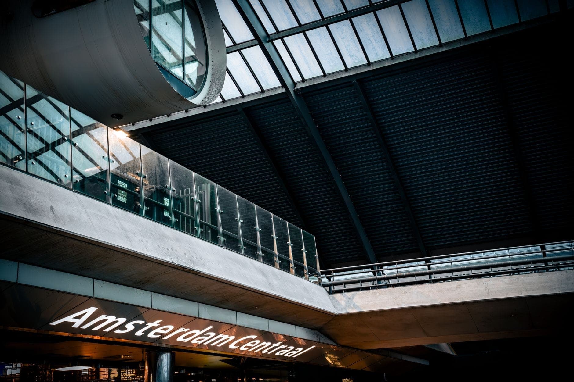Modernes Glasdach und Innenbeschilderung des Bahnhofs Amsterdam Centraal, mit einem Teil des Stationsnamens sichtbar und guter Beleuchtung.