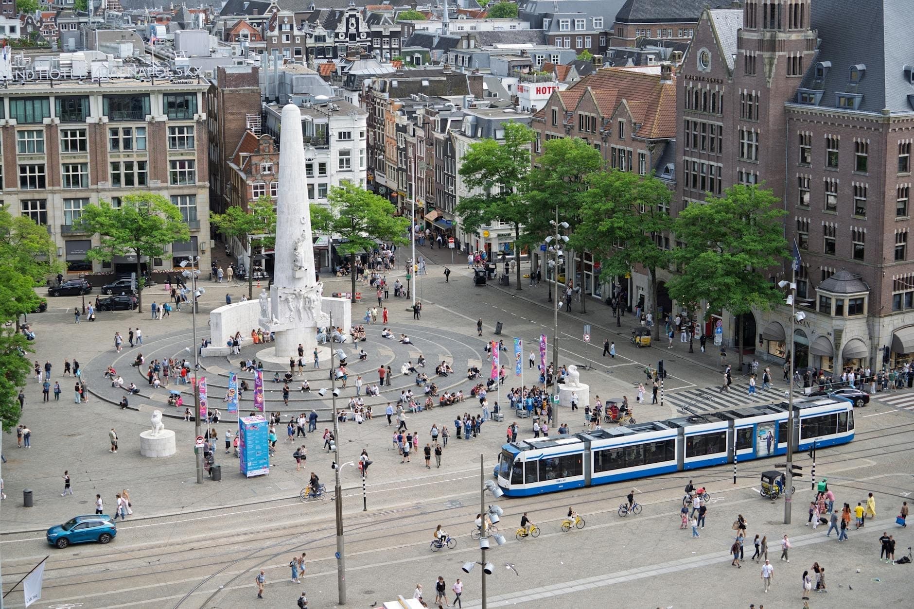 Luftaufnahme des Dam Square in Amsterdam mit dem National Monument, Straßenbahnen, Fußgängern und historischen Gebäuden im Stadtzentrum.