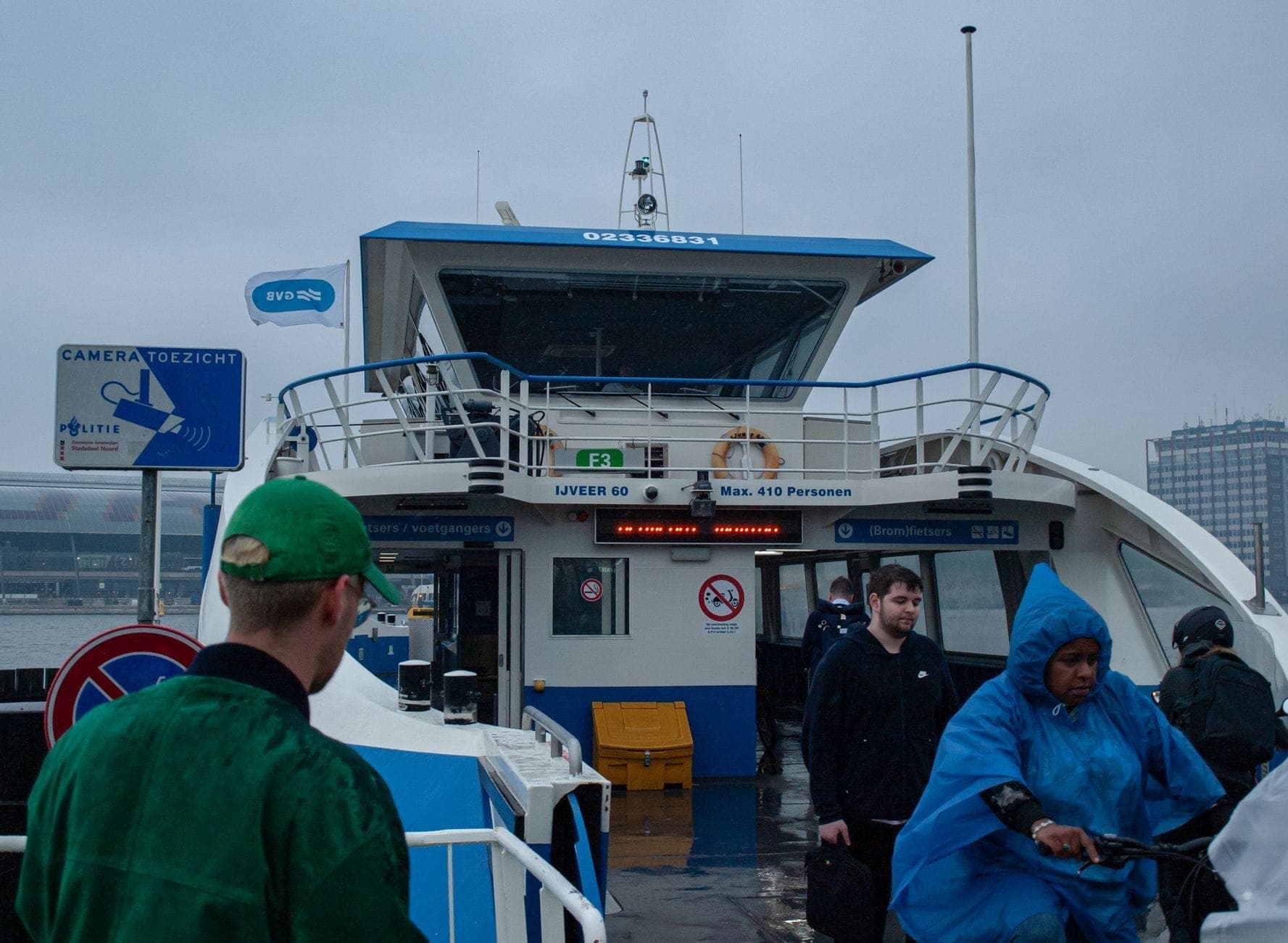 Menschen, die an einem bewölkten Tag von einer GVB-Fähre in Amsterdam-Noord aussteigen, mit dem Fähranleger gut sichtbar im Hintergrund.