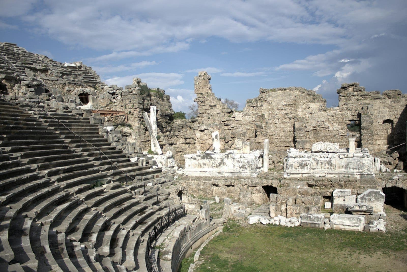 Weiter Blick auf ein antikes römisches Theater mit Steinsitzen und Ruinen unter leicht bewölktem Himmel – ein eindrucksvolles Zeugnis der historischen Stätten Antalyas.