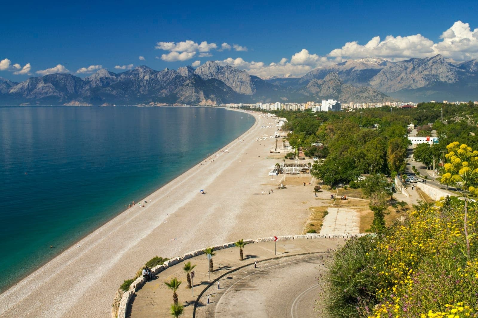 Ein atemberaubender Strand in Antalya mit ruhigem türkisfarbenem Wasser, Bergen in der Ferne und strahlend blauem Himmel – ein Paradies für Besucher der türkischen Küste.