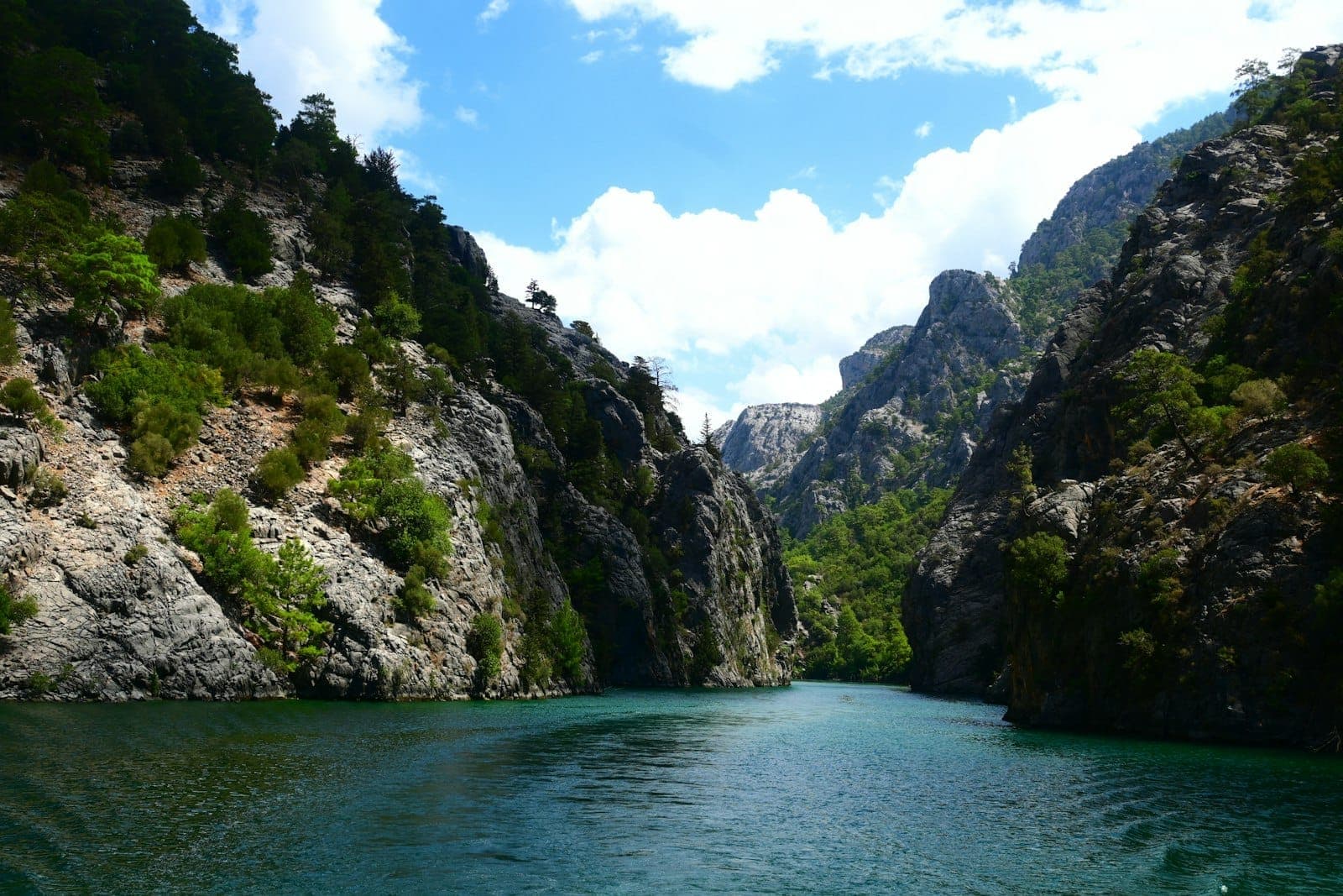 Klarer türkisfarbener Fluss, der sich durch einen dramatischen Felscanyon mit üppig grünen Bäumen unter einem strahlend blauen Himmel in der Wildnis von Antalya schlängelt.