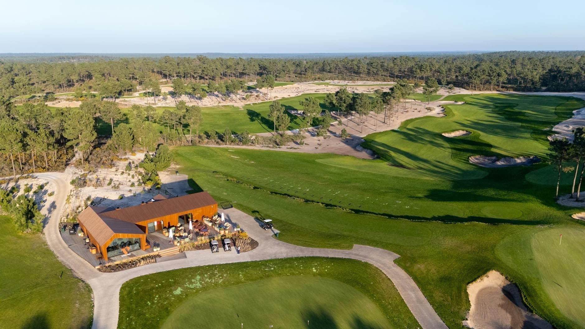 Luftaufnahme eines üppigen Golfplatzes in einem bewaldeten Gebiet mit einem Clubhaus, grünen Fairways, Bäumen und Sandbunkern.
