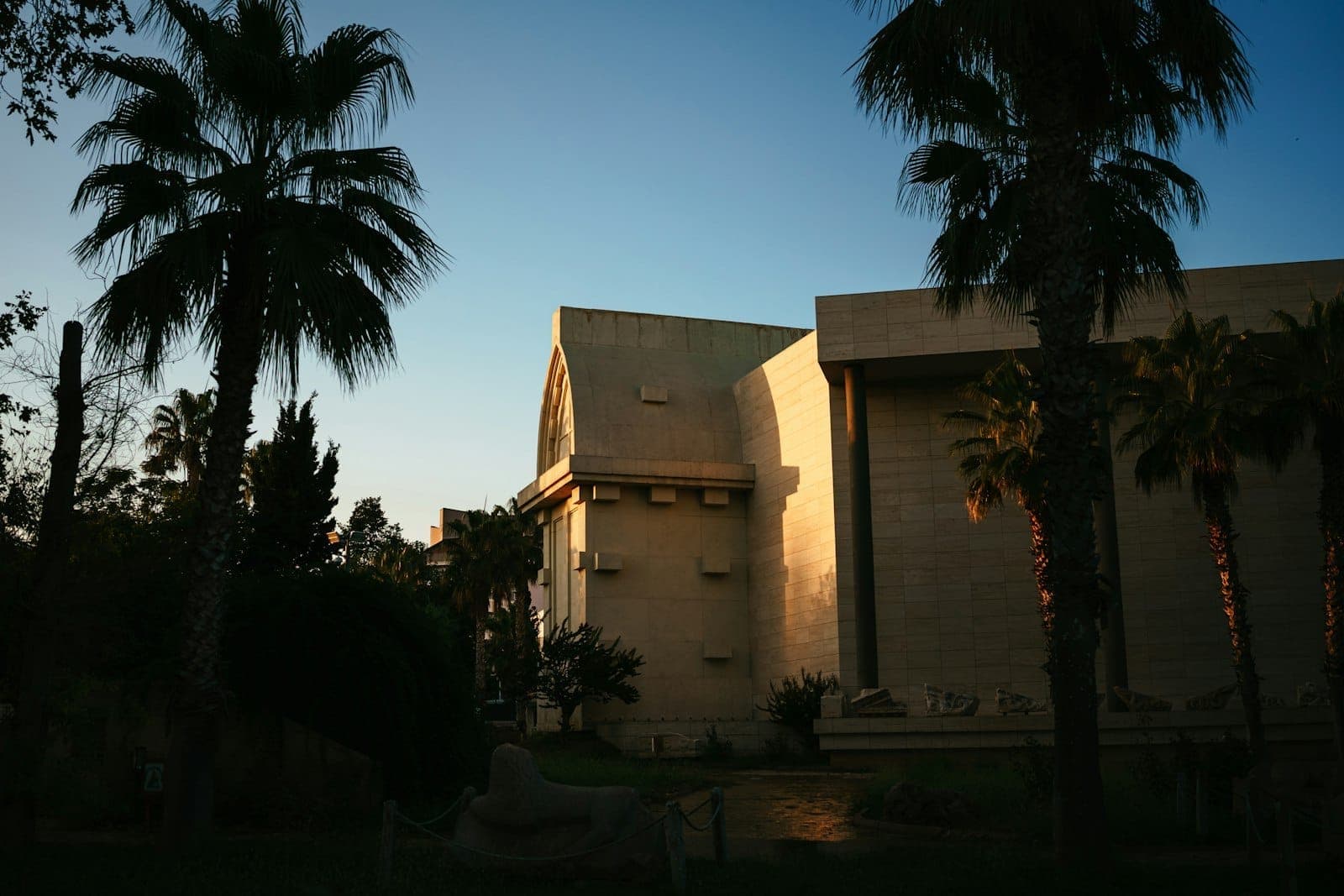 Vue extérieure du bâtiment du Musée d'Antalya partiellement dans l'ombre, entouré de palmiers dans la lumière de fin d'après-midi.