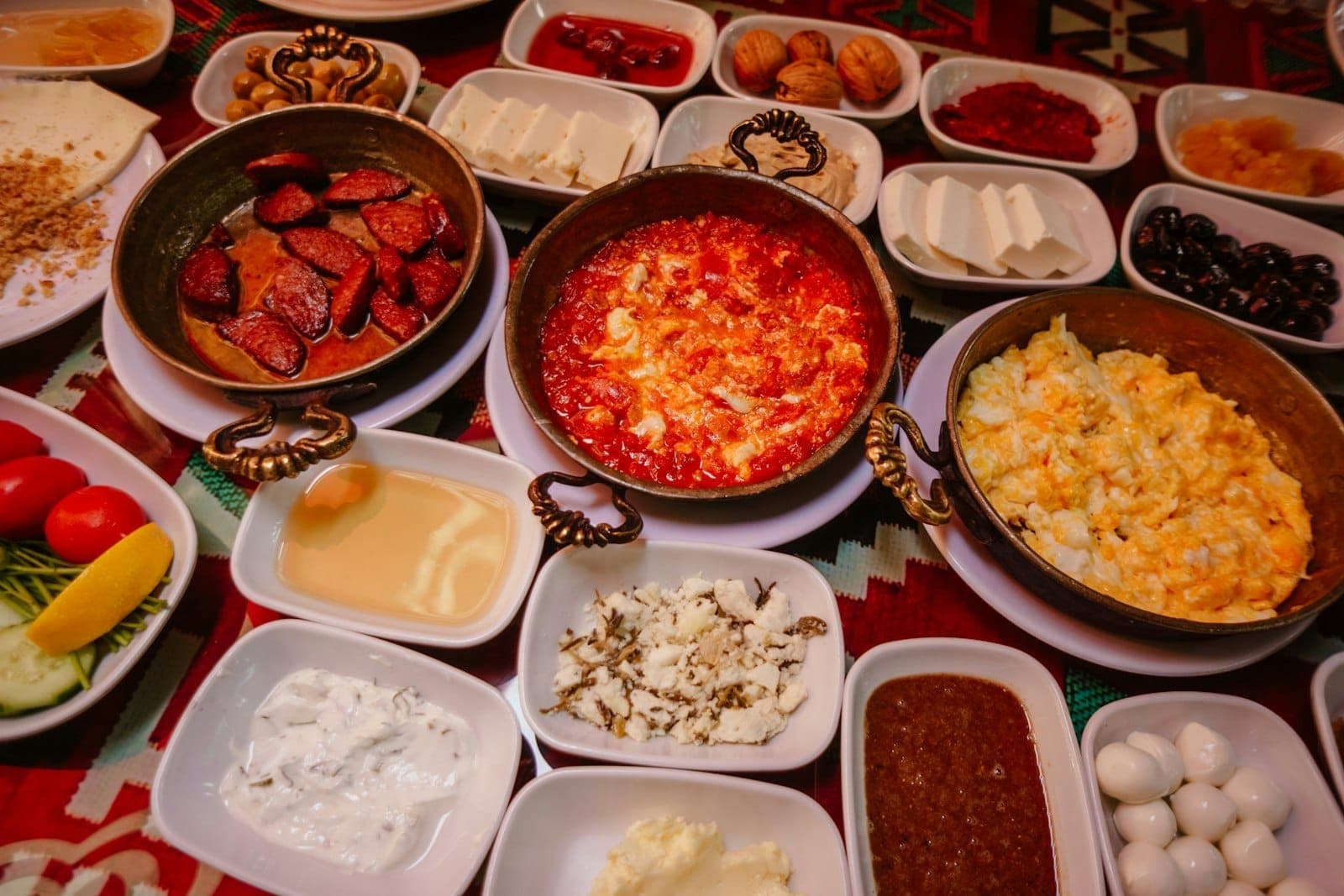 Un petit-déjeuner turc coloré avec de petits plats d'œufs, de fromage, d'olives, de pains et de tartinades disposés sur une nappe à motifs.