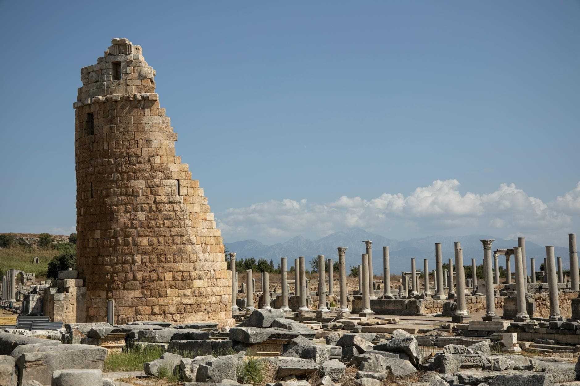Antiker Steinturm und Kolonnadenruinen unter blauem Himmel an einer historischen Stätte bei Antalya.
