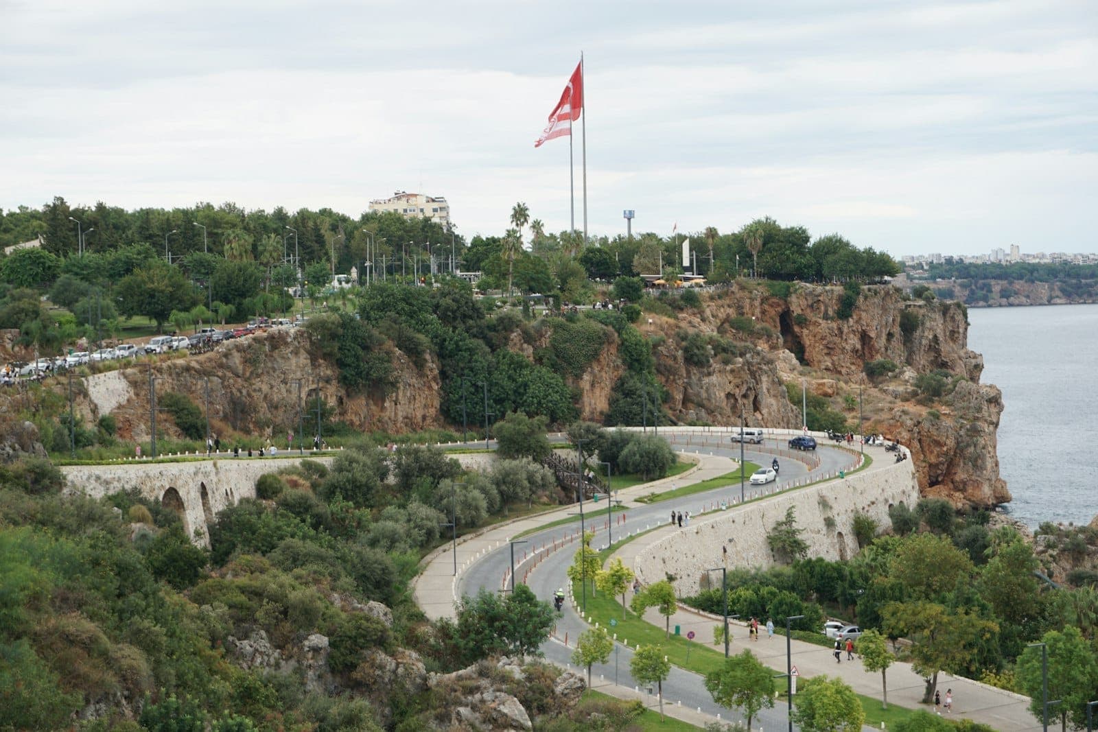 Park auf einer Klippe mit Blick aufs Meer, mit Wegen, Grünflächen, Spaziergängern und einer großen türkischen Flagge nahe der Küste von Antalya.
