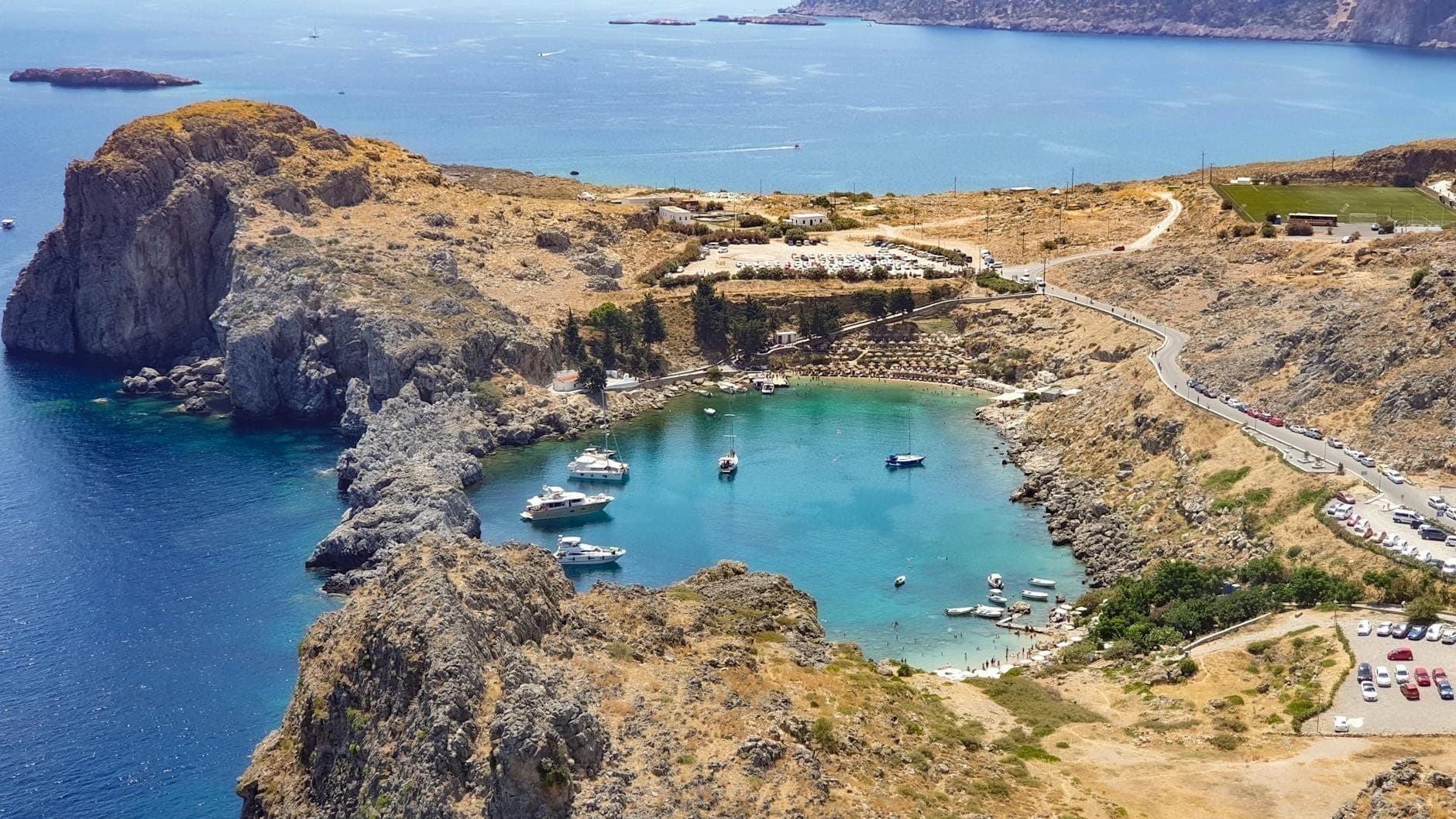 Widok z lotu ptaka na zatokę Anthony Quinn Bay na Rodos, z turkusową wodą, łodziami, skalistą linią brzegową i bujną zielenią.