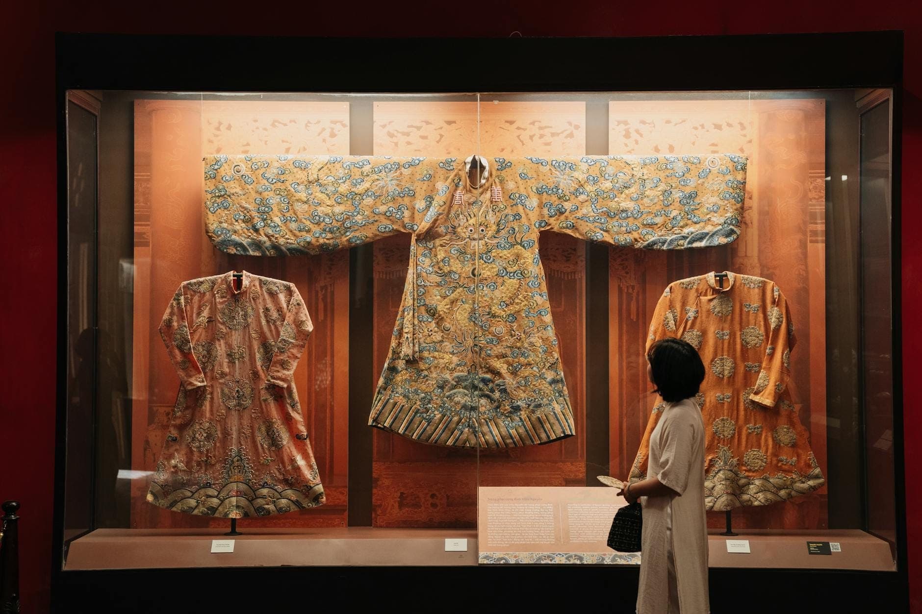 Un visiteur observe des tenues traditionnelles áo dài richement brodées exposées dans une vitrine au Áo Dài Museum de Ho Chi Minh City.