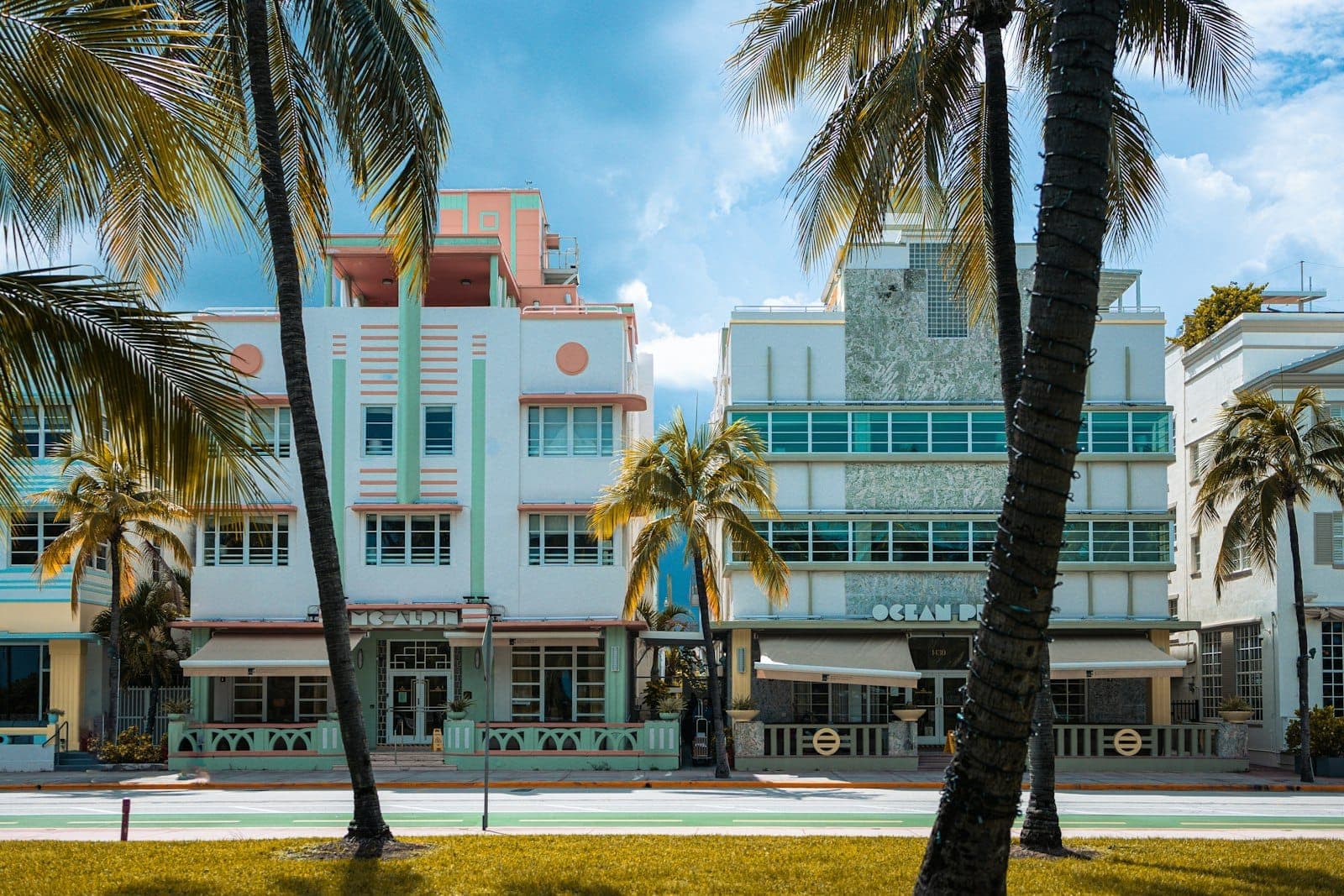 Colorful pastel Art Deco buildings with palm trees in front, clear sky above, on Ocean Drive in Miami Beach's historic Art Deco District.