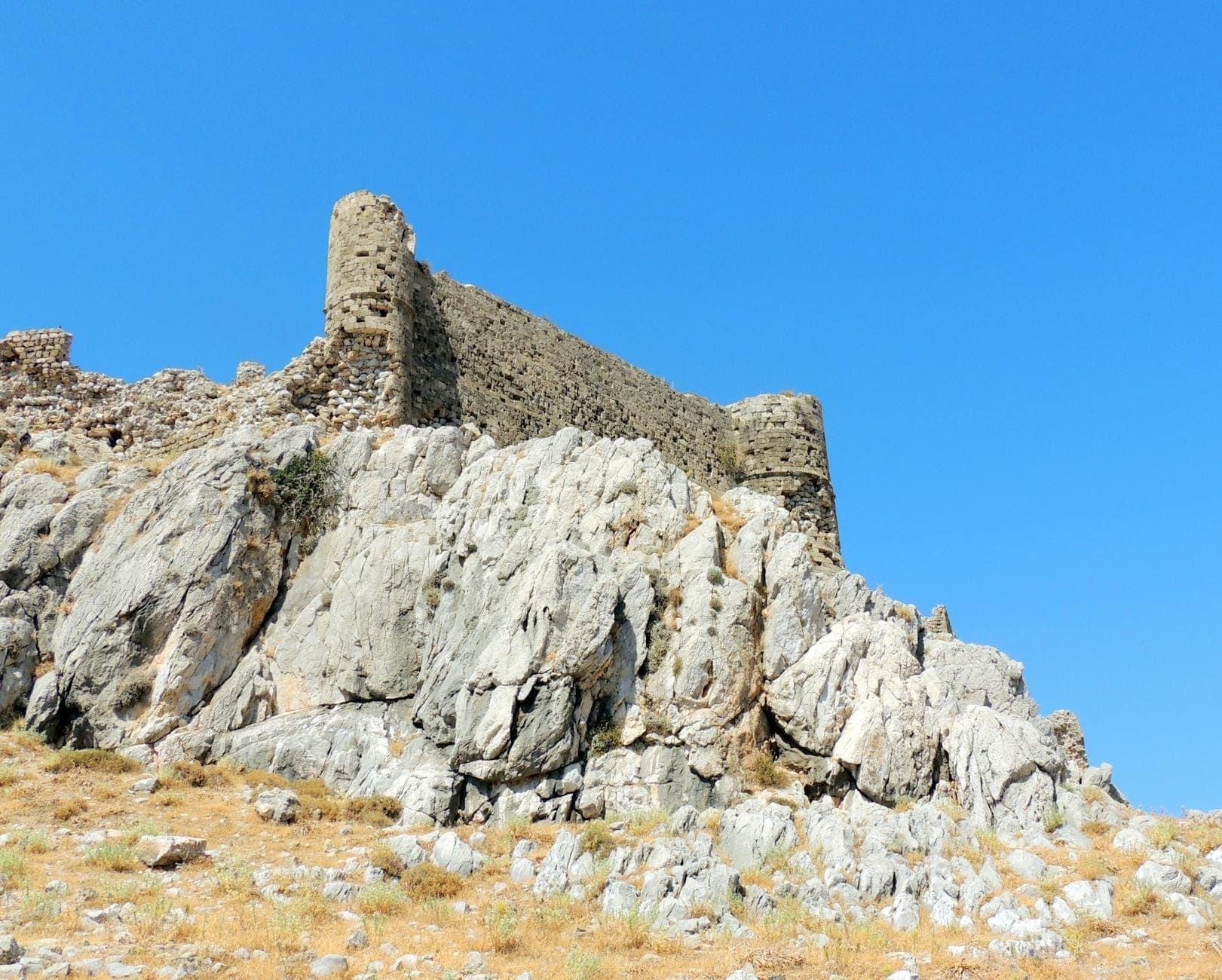 Ruines d'un château médiéval en pierre perchées au sommet d'une crête calcaire accidentée, sous un ciel bleu intense, évoquant mystère historique et esprit d'aventure.