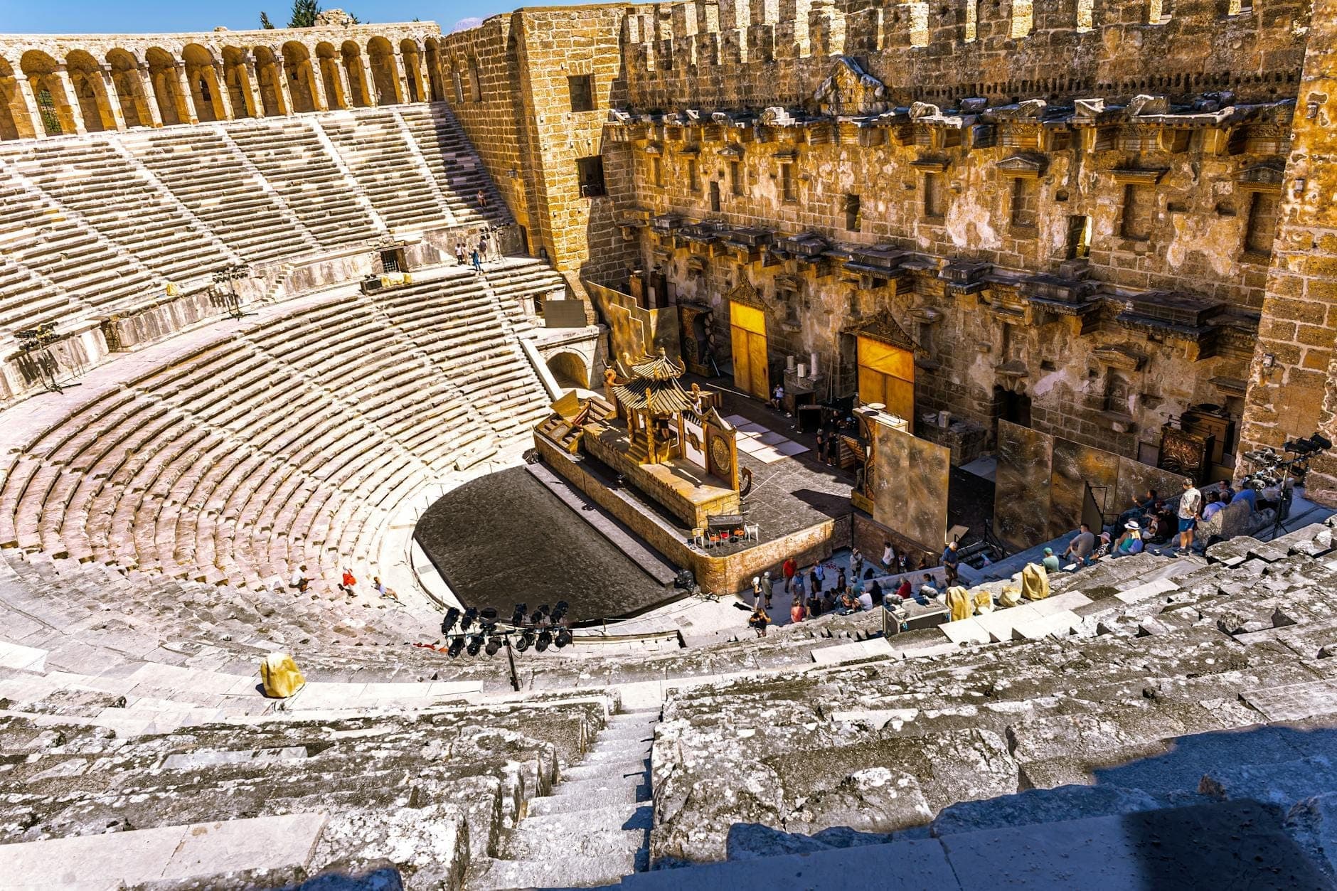 Weitwinkelansicht des Antiken Theaters von Aspendos mit aufgebautem Bühnenbild, besetzten Zuschauerrängen und leuchtendem goldenem Licht im besterhaltenen römischen Amphitheater.