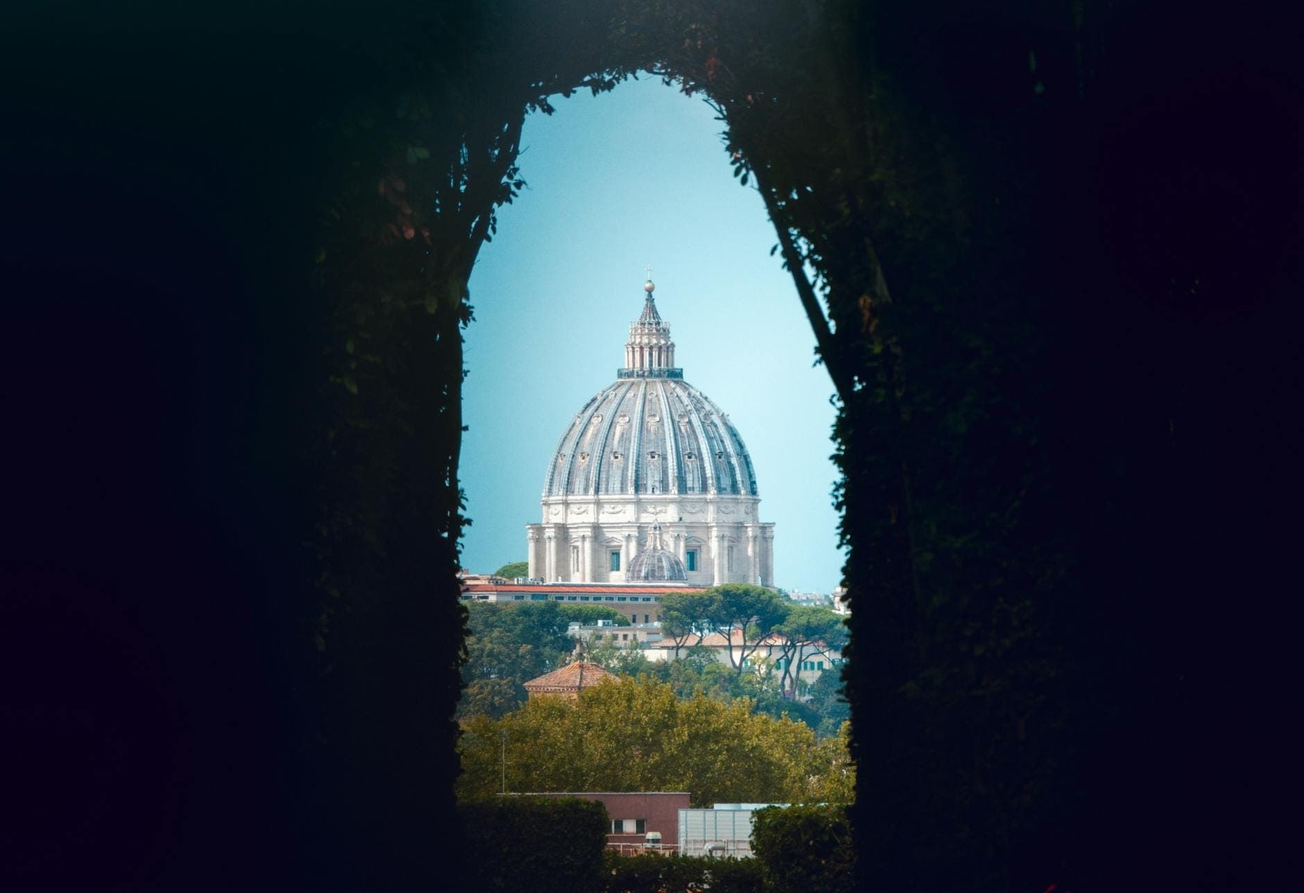 Tanaw sa pamamagitan ng Aventine Keyhole na nagpapakita ng simboryo ng Basilika ni San Pedro nang perpektong nakasentro, napapalibutan ng maitim na mga bakod at maliwanag na kalangitan ng Roma.
