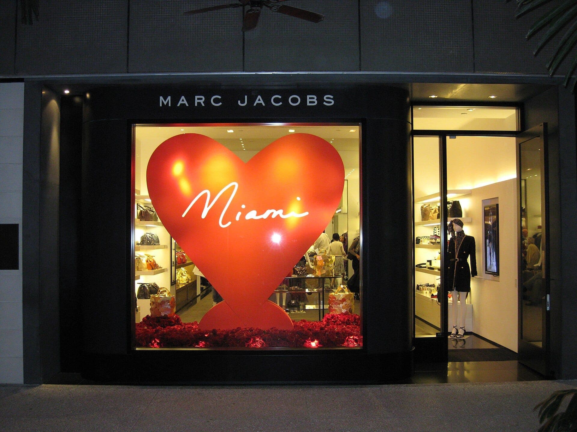 La devanture de la boutique Marc Jacobs aux Bal Harbour Shops présente un grand cœur rouge avec 'Miami' inscrit à l'intérieur, illuminée la nuit avec des vitrines chics.
