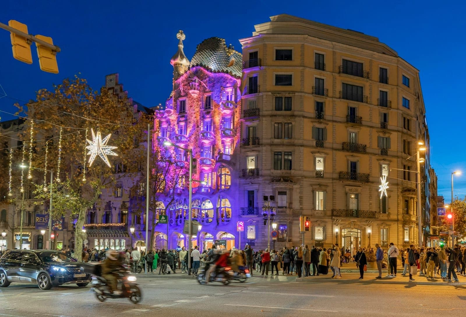 Casa Batlló am Passeig de Gràcia nachts mit bunten Lichtern beleuchtet, umgeben von Menschen und lebhaftem Stadtleben in Barcelona.