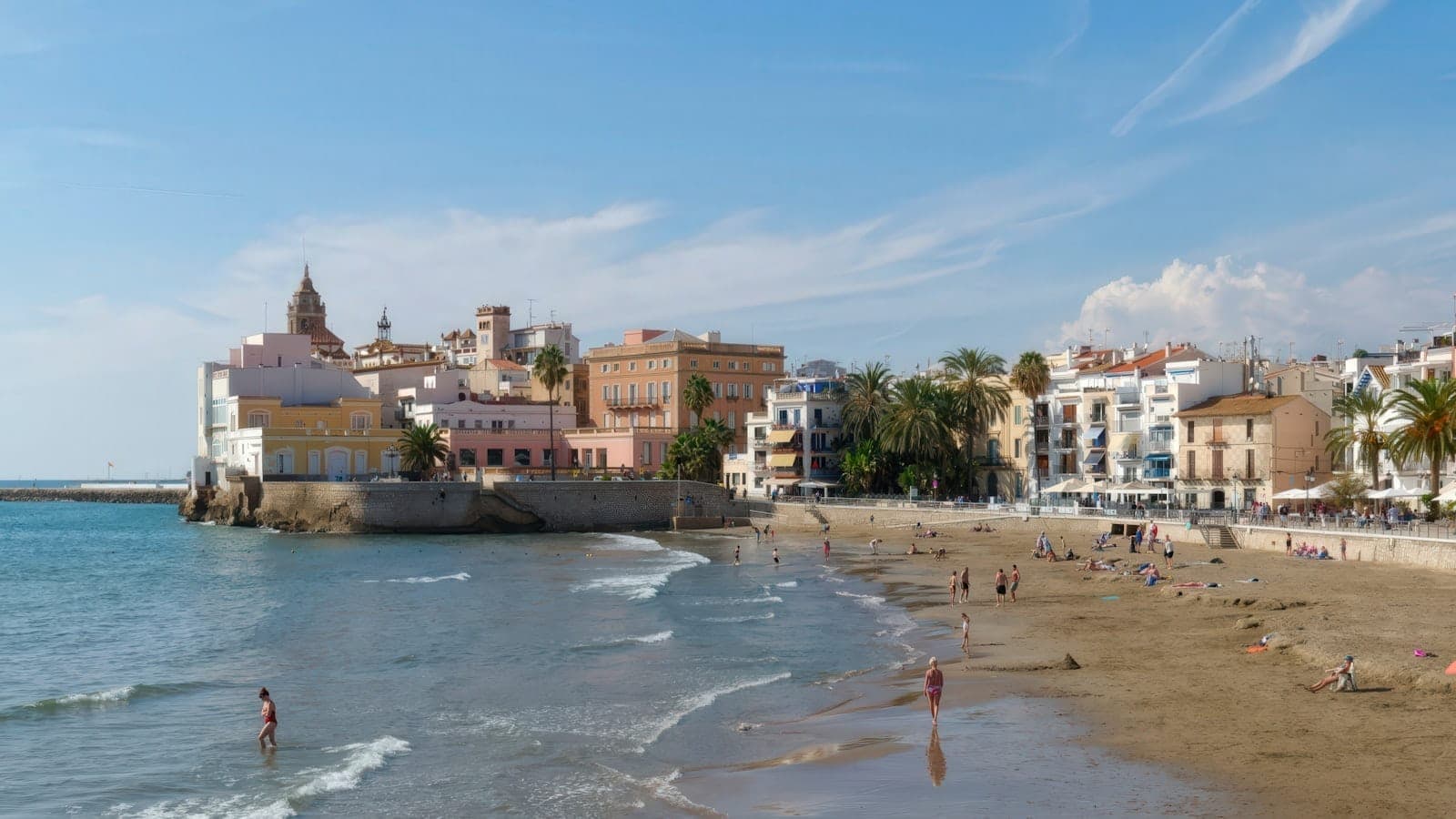 Kolorowe budynki i kościół z widokiem na piaszczystą plażę i spokojne morze w Sitges niedaleko Barcelony pod bezchmurnym błękitnym niebem.