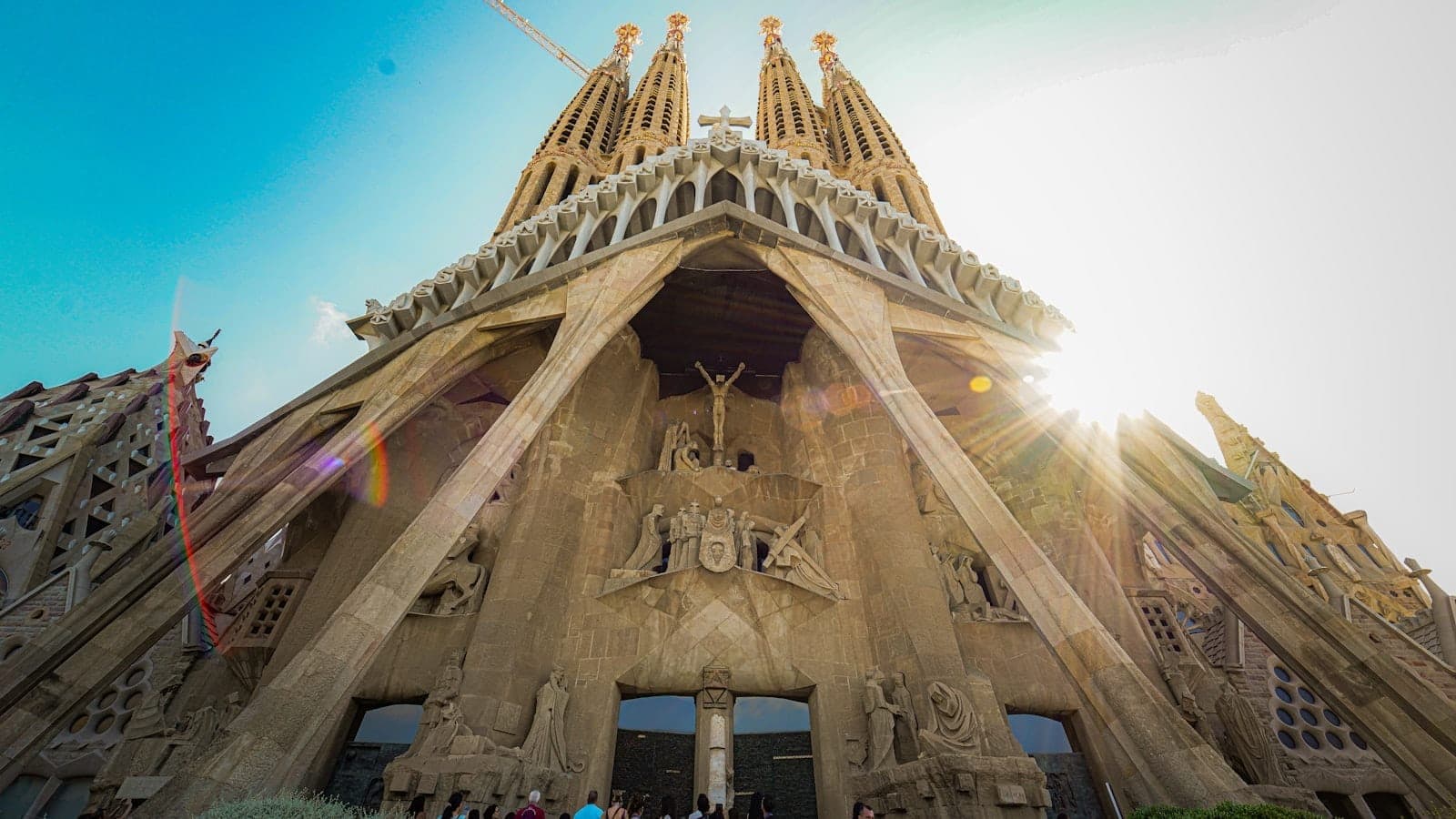Sagrada Família cephesinin alçak açılı görünümü, güneş ışığı ve açık gökyüzü altında karmaşık mimarisi ve inşaat halindeki yüksek kulelerini gösteriyor.