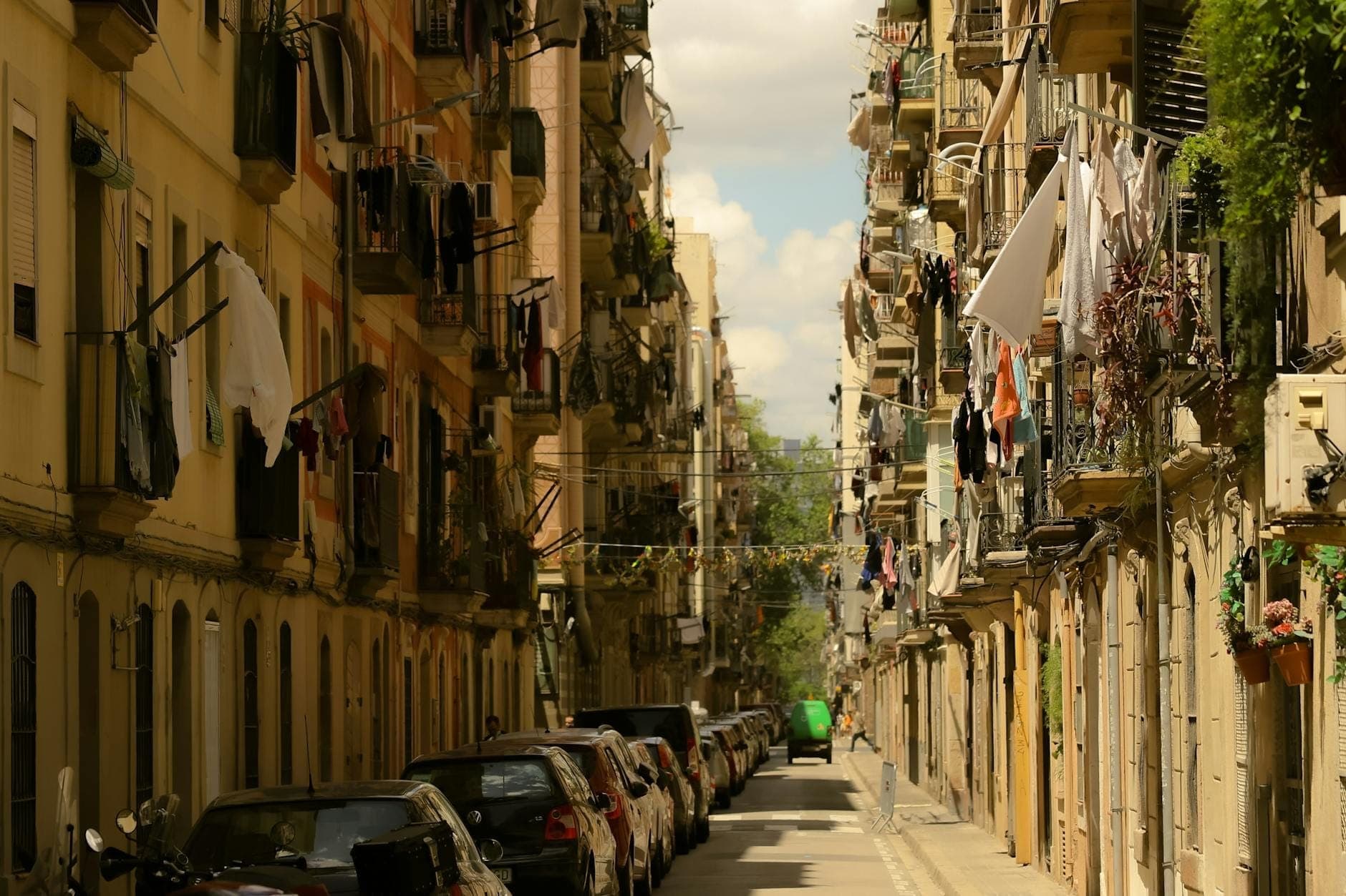 Calle estrecha de Barcelona flanqueada por antiguos edificios de apartamentos, ropa tendida en los balcones y coches aparcados a ambos lados.