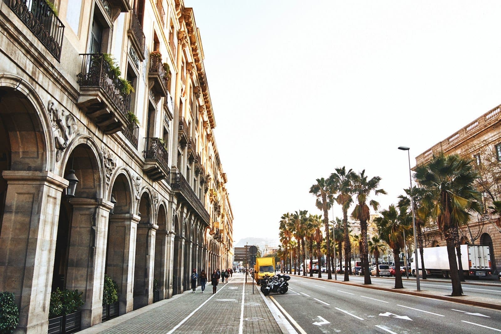 Bulevar soleado en Barcelona con elegantes arcadas, palmeras y personas paseando: un animado ambiente urbano que atrae a todas las edades.