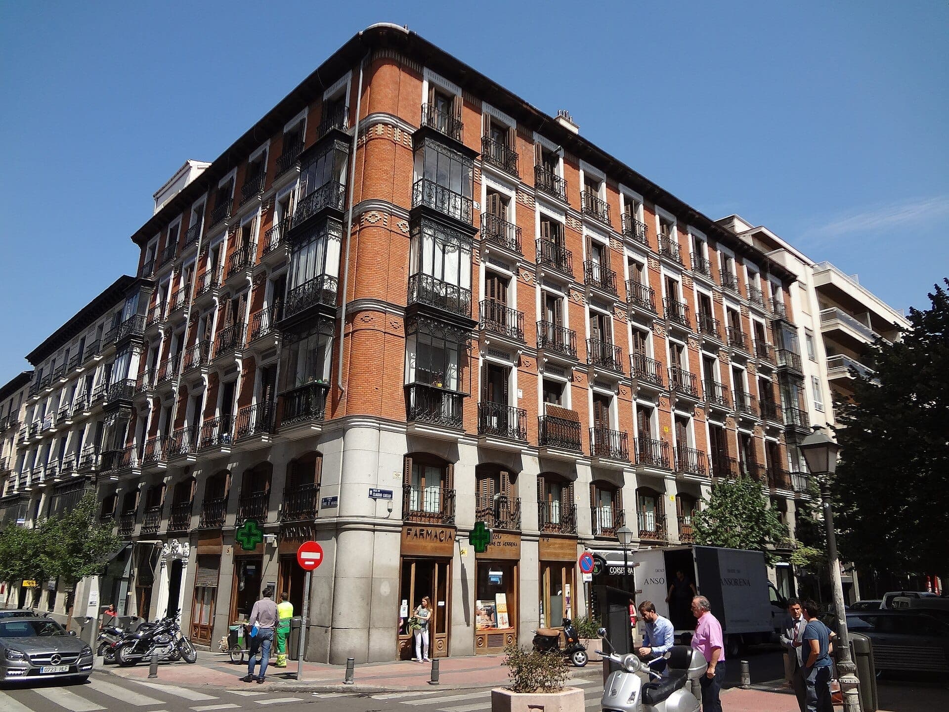 วิวถนนของอาคารที่พักอาศัยอิฐแดงสไตล์คลาสสิกใน Barrio de Salamanca กรุงมาดริด พร้อมระเบียงเหล็กดัดและร้านค้าชั้นล่างในวันที่แดดจัด