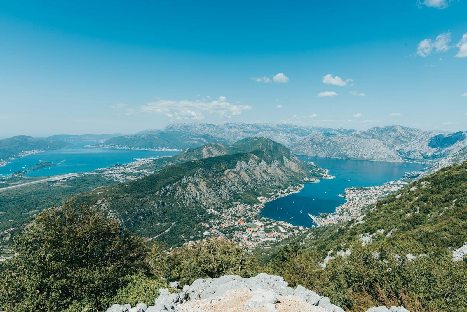Large vue panoramique de la Baie de Kotor avec des montagnes spectaculaires, des eaux bleues et la ville de Kotor visible, illustrant parfaitement le paysage idéal pour les excursions en bateau.