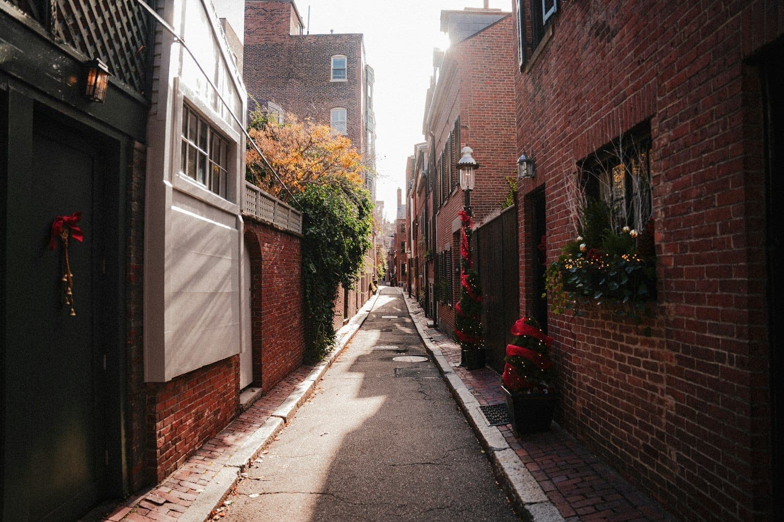 Ruelle en brique baignée de soleil à Beacon Hill, bordée de maisons historiques en brique rouge, de portes décorées et de jardinières fleuries, capturant l'atmosphère charmante du quartier.