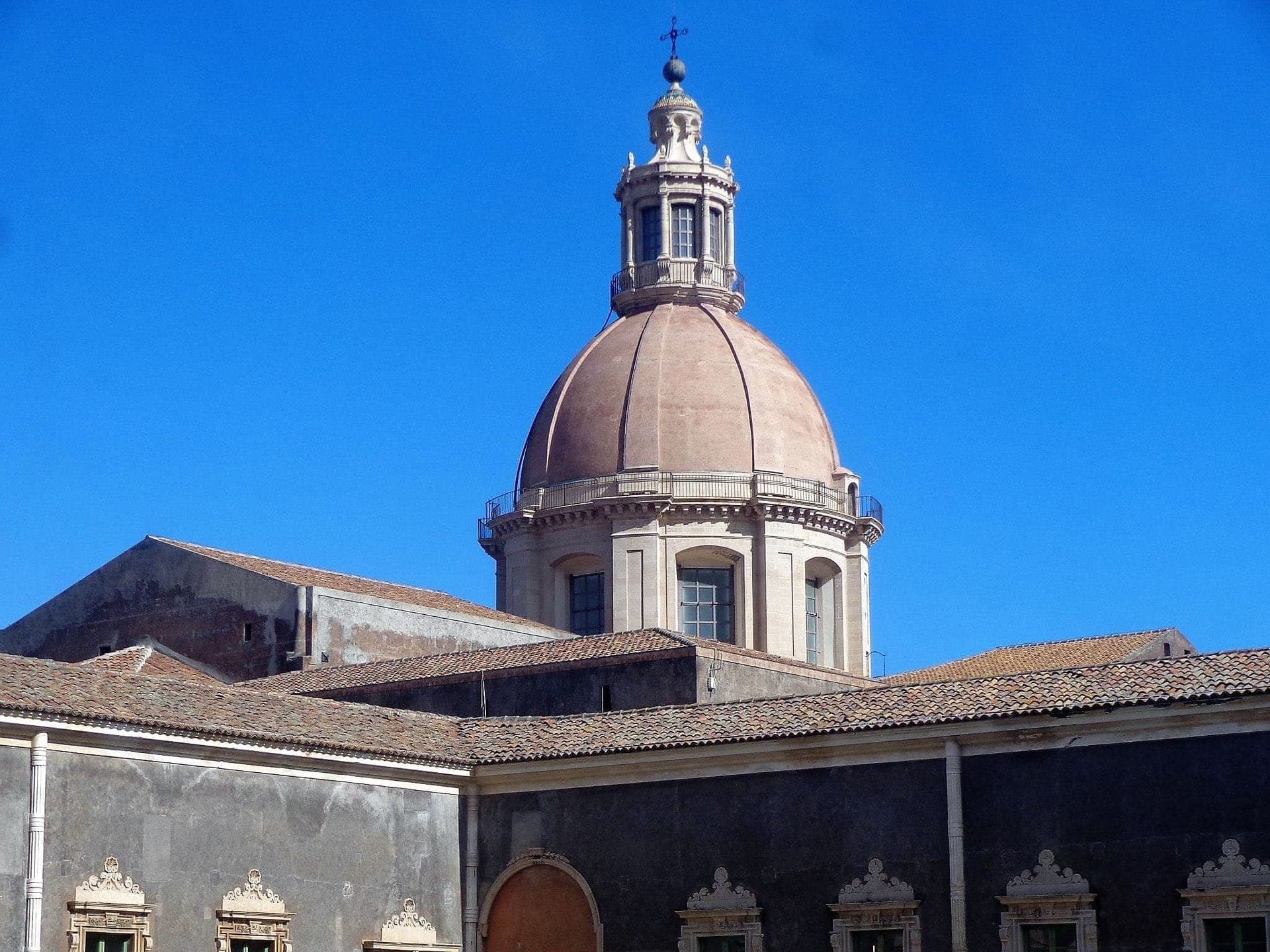 Atap berkubah dan arsitektur barok Biara Benediktin San Nicolò l'Arena di bawah langit biru cerah di Catania.