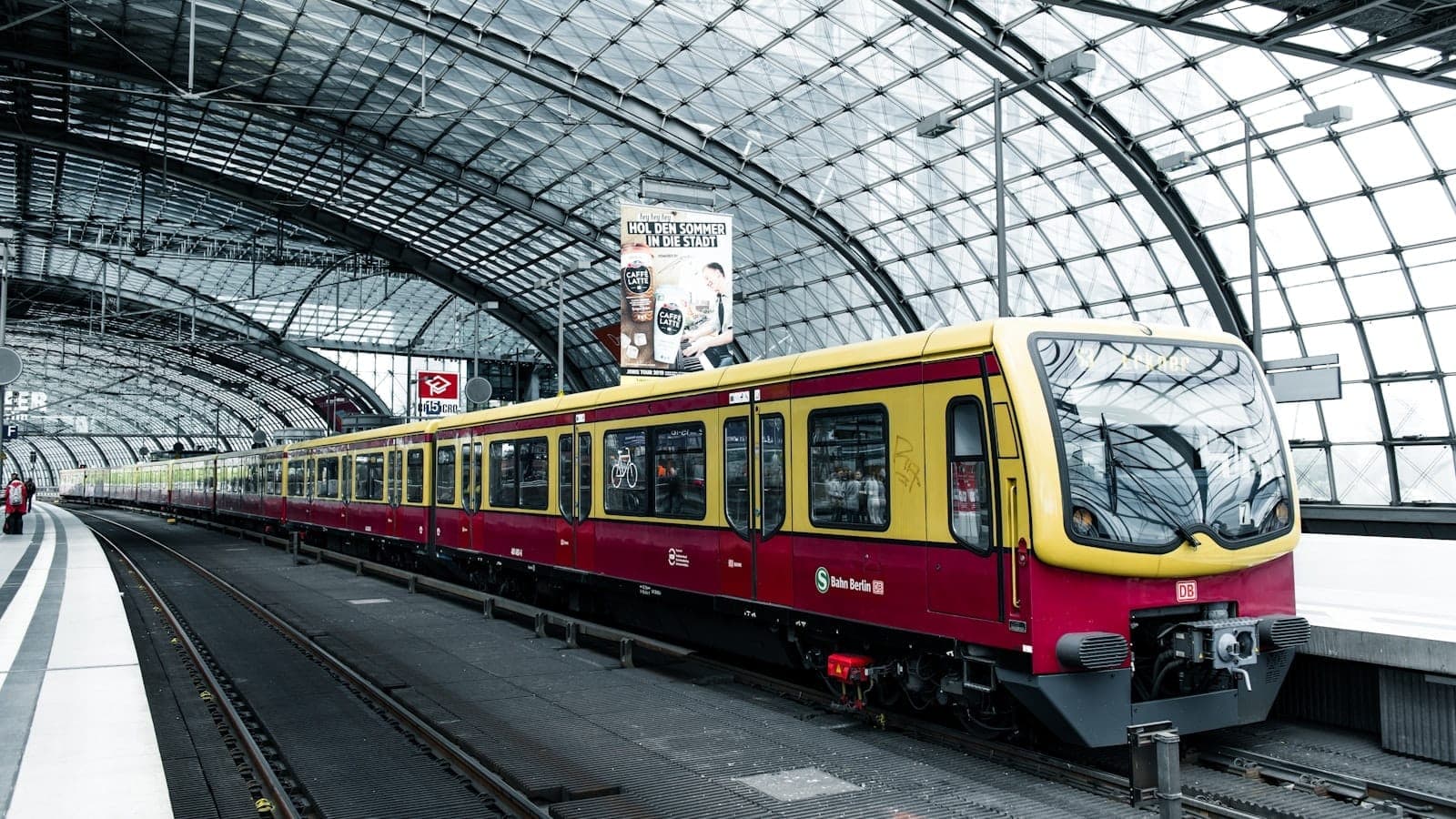 Moderner S-Bahn-Zug auf dem Bahnsteig der Berlin Hauptbahnhof mit gewölbtem Glasdach und wartenden Fahrgästen an einem hellen Tag
