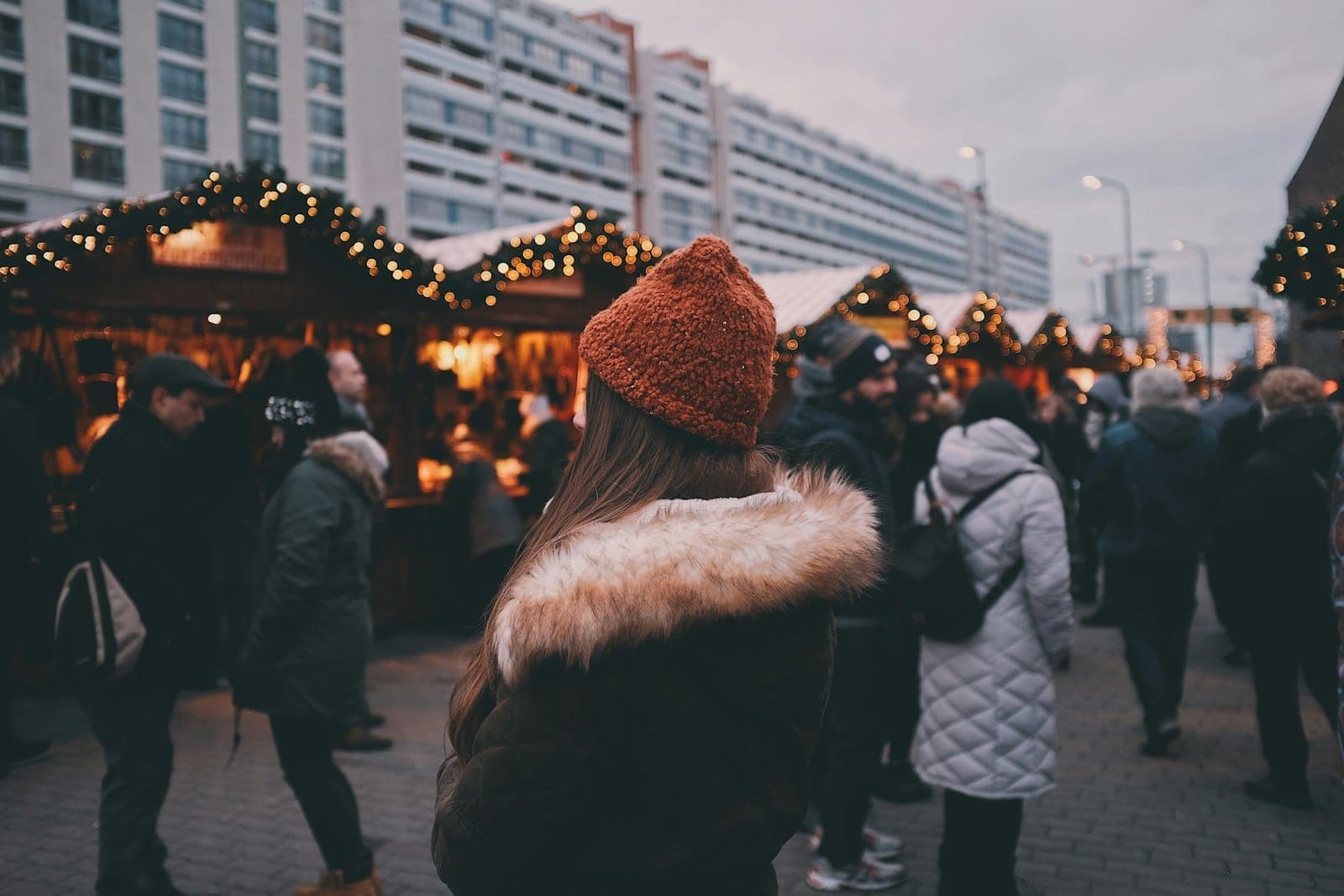 Menschen in Wintermänteln genießen den Berliner Weihnachtsmarkt mit festlicher Beleuchtung und Holzbuden im Freien.