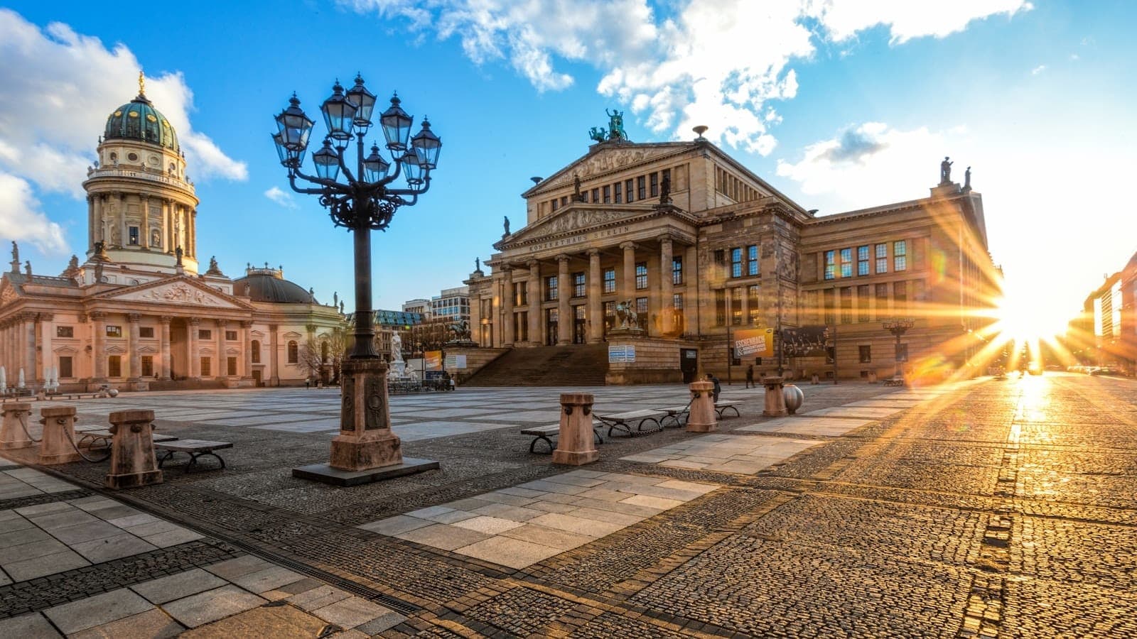 Weitläufige Aussicht auf den Gendarmenmarkt bei Sonnenuntergang mit dem Konzerthaus und dem Dom Berlins, mit leerem Platz, wo normalerweise die Stände des Weihnachtsmarkts aufgebaut werden.