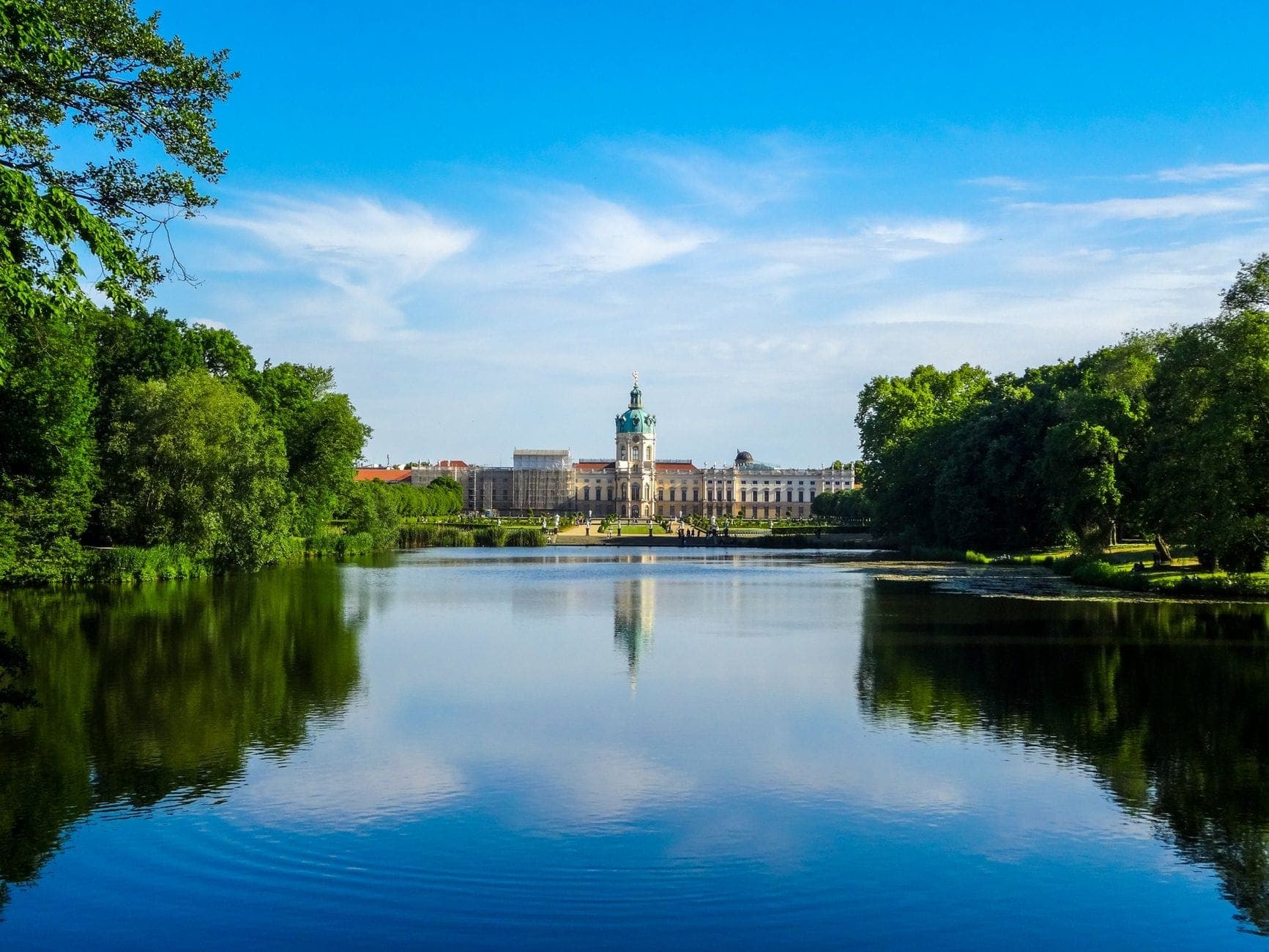 วิวข้ามทะเลสาบอันสงบสู่พระราชวัง Charlottenburg ในเบอร์ลิน ล้อมรอบด้วยต้นไม้เขียวชอุ่มภายใต้ท้องฟ้าสีฟ้าสดใส