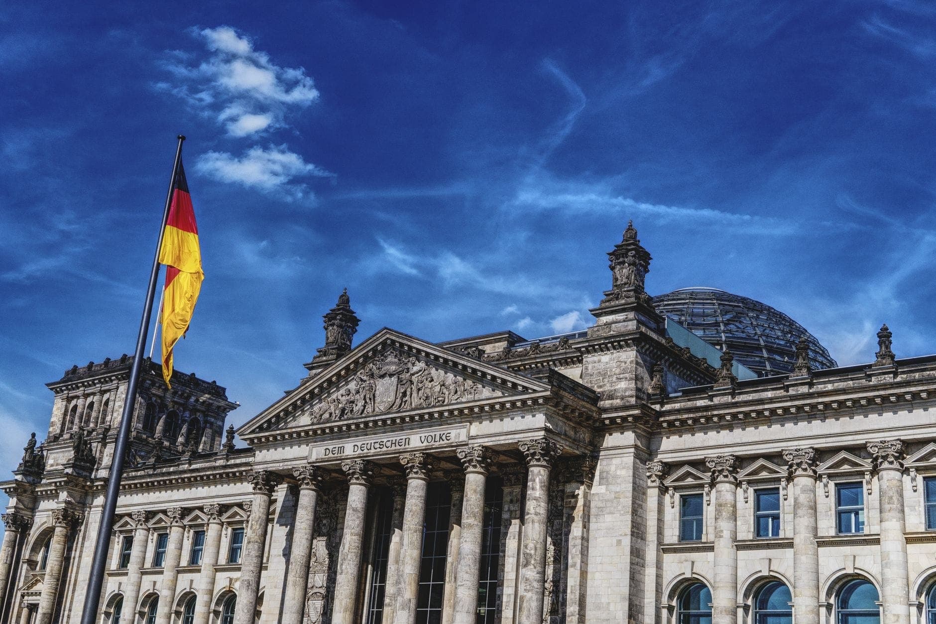 The Reichstag building in Berlin with German flag and glass dome under a vivid blue sky, symbolizing German history and identity.