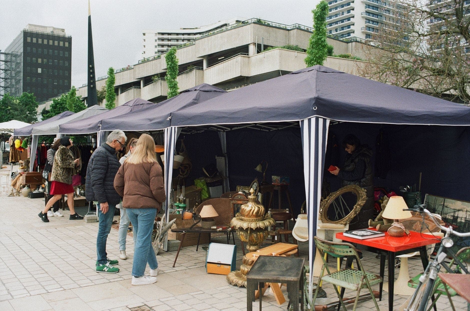 Mercato delle pulci all'aperto a Berlino con acquirenti che esplorano le bancarelle, edifici moderni sullo sfondo, tipico della vita di strada estiva e delle attività stagionali.