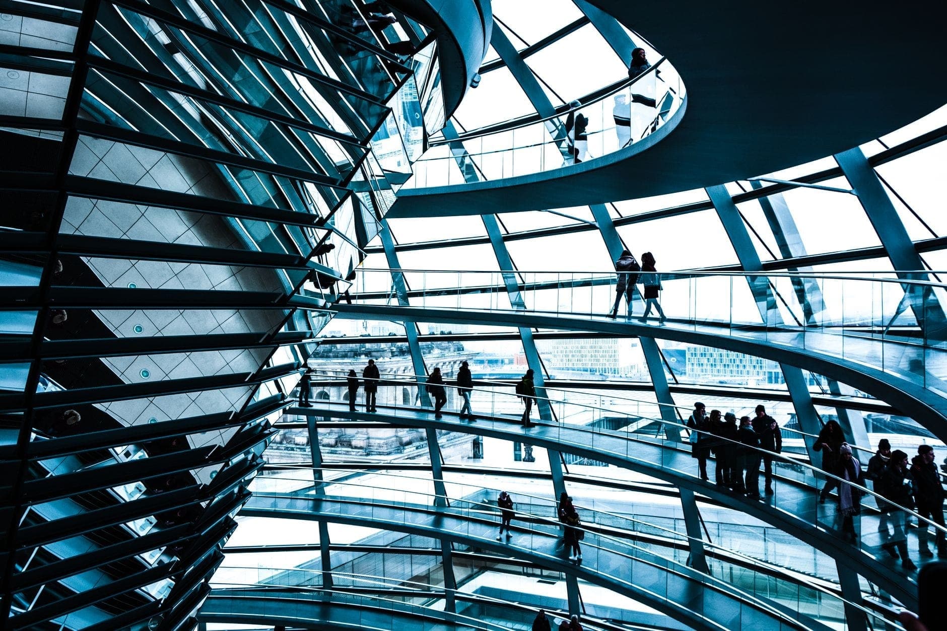 Vista interna della cupola del Reichstag di Berlino con numerosi visitatori che camminano sulle rampe a spirale e osservano l'architettura e le vedute della città.