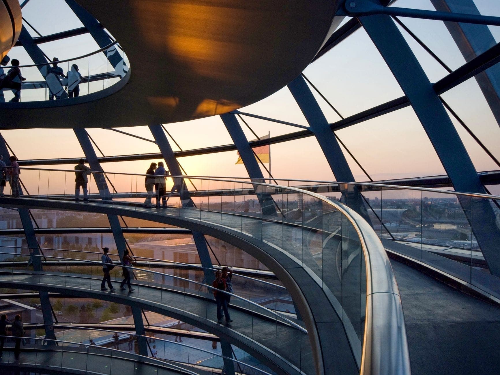 ผู้คนเดินอยู่ภายในโดมของ Reichstag ในเบอร์ลินช่วงพระอาทิตย์ตก พร้อมวิวกระจกแบบพาโนรามาและสถาปัตยกรรมสมัยใหม่