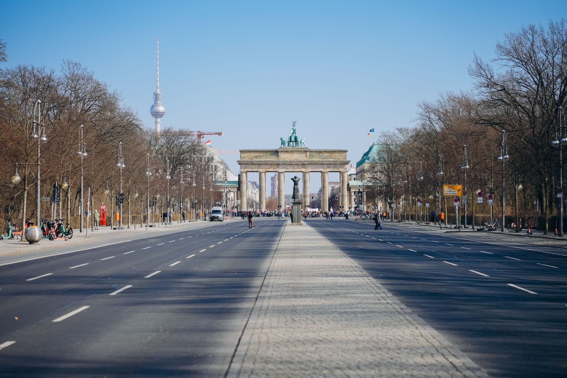 มุมมองกว้างระดับถนนลงไปตาม Unter den Linden สู่ Brandenburg Gate โดยมี Berlin TV Tower มองเห็นได้ในพื้นหลังและผู้คนในระยะไกล