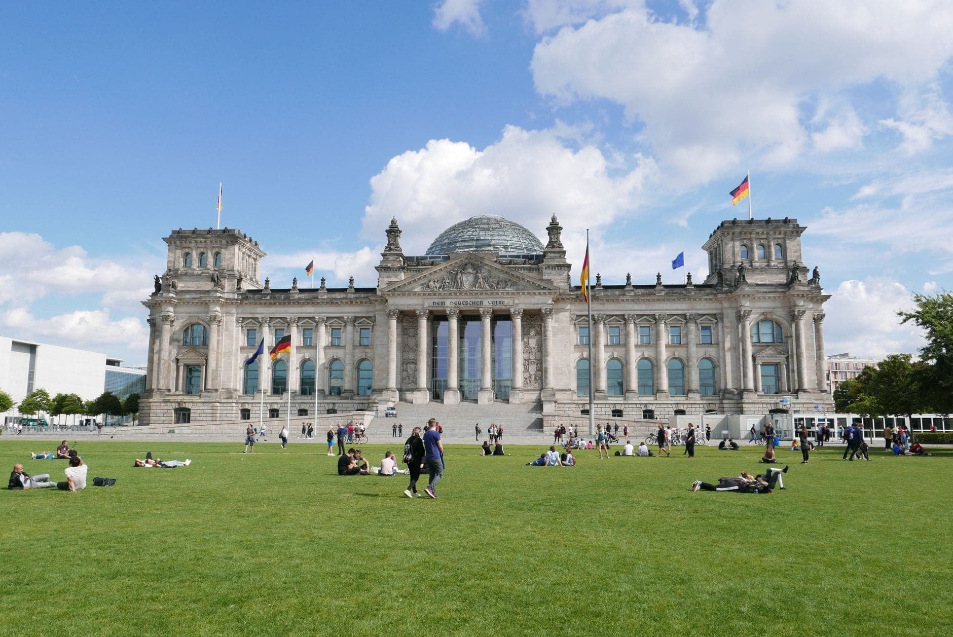 Weitwinkelansicht des Reichstagsgebäudes mit Menschen, die sich auf dem grünen Rasen unter blauem Himmel entspannen und spazieren gehen, Berlin.
