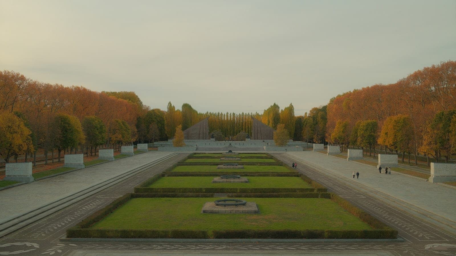 Weitwinkelansicht des Sowjetischen Ehrenmahls im Treptower Park in Berlin mit baumgesäumten Wegen und grünen Rasenflächen im Herbst.
